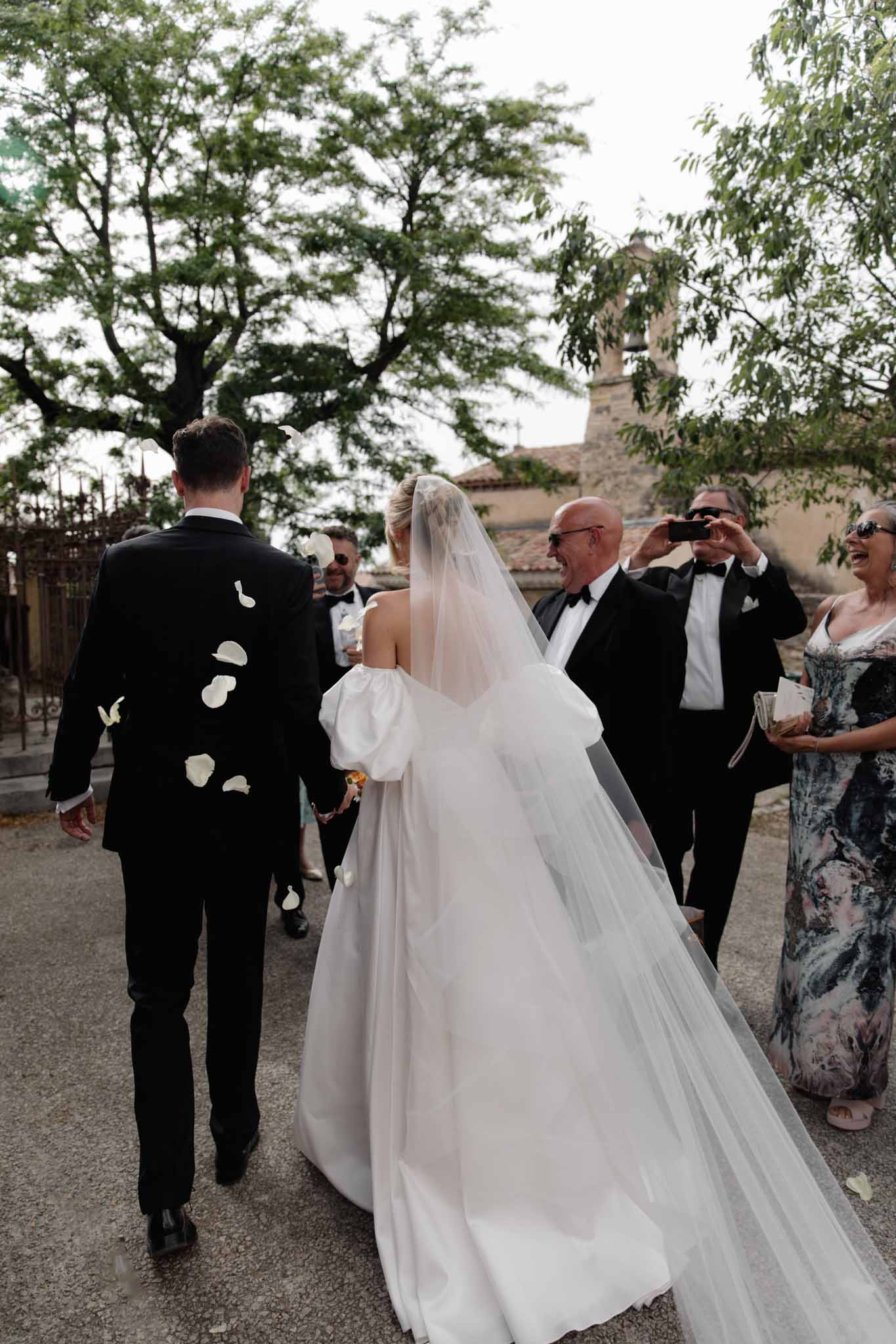 Bride and groom recessional on stone pathway with white confetti under tree canopy at historic estate