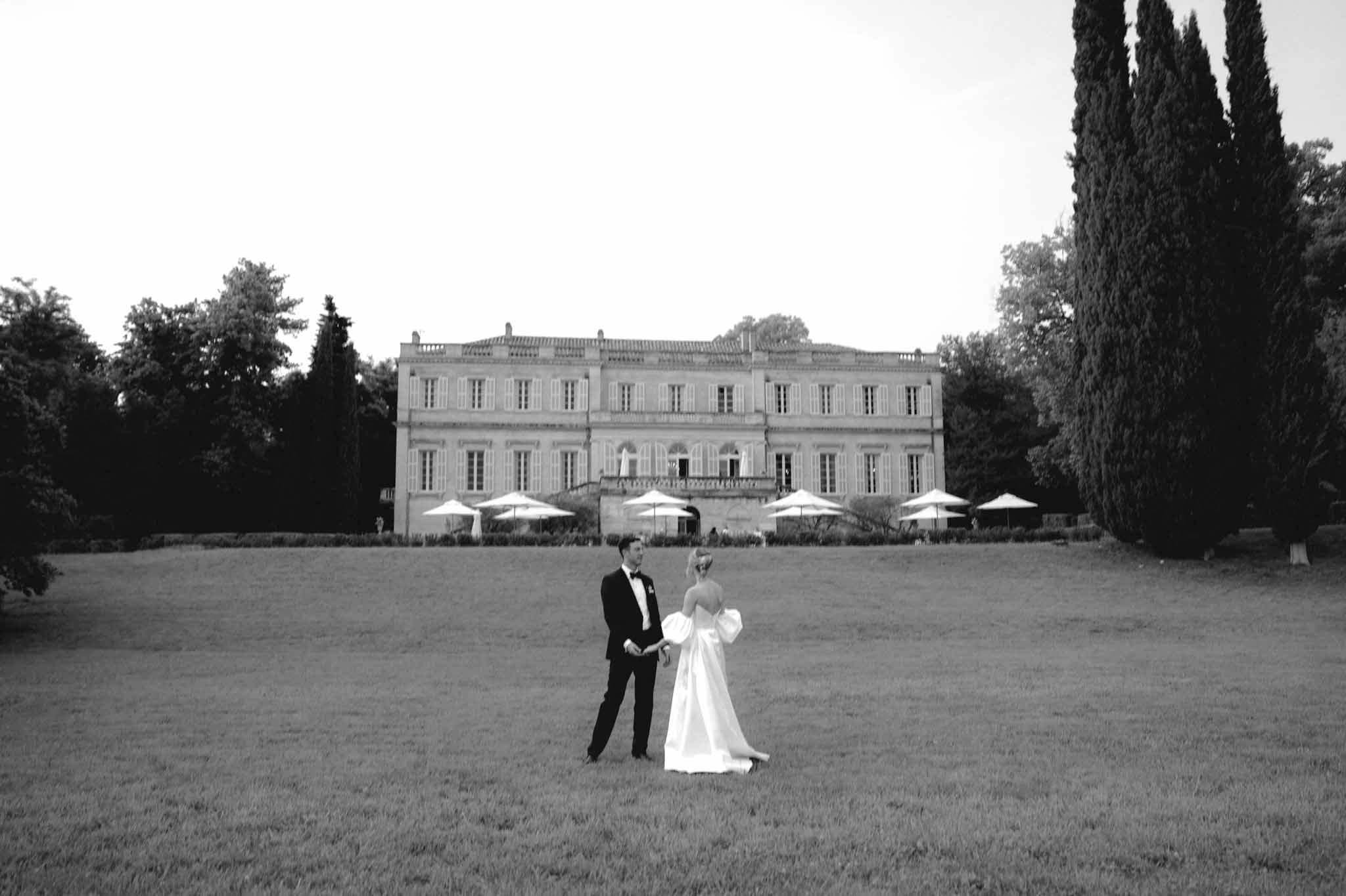 Black-and-white couple before neoclassical mansion with cypress trees and white umbrellas on terrace