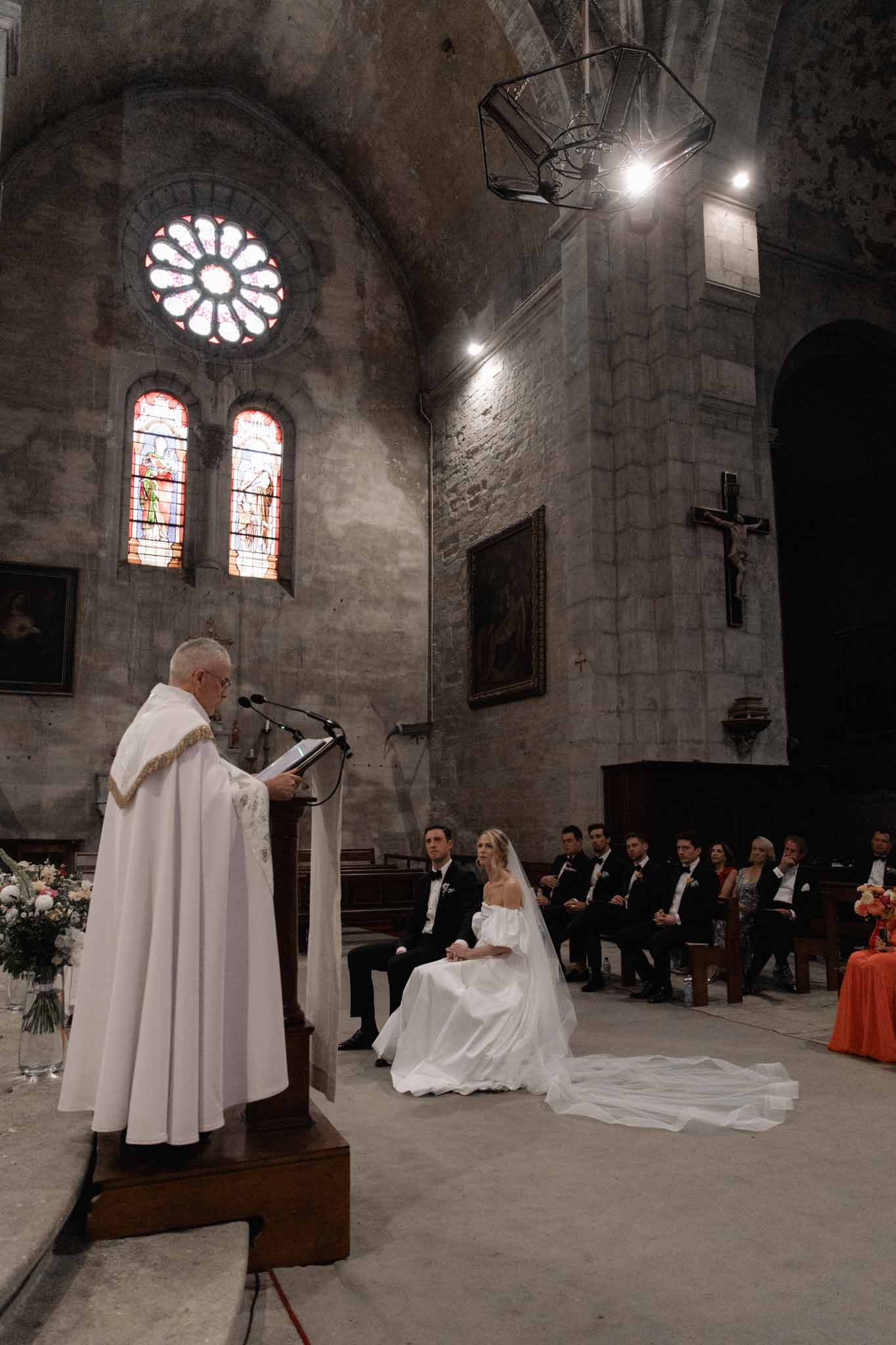 Wedding ceremony in stone Gothic chapel, officiant at lectern, bride in ivory ballgown, bridesmaids in rust dresses