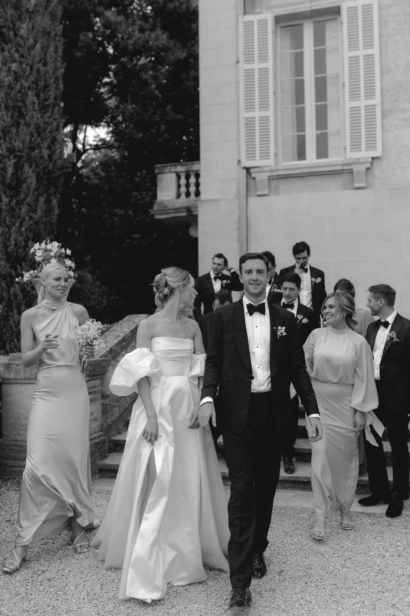 Black and white recessional with bride and groom walking flanked by bridal party outside a classical European villa