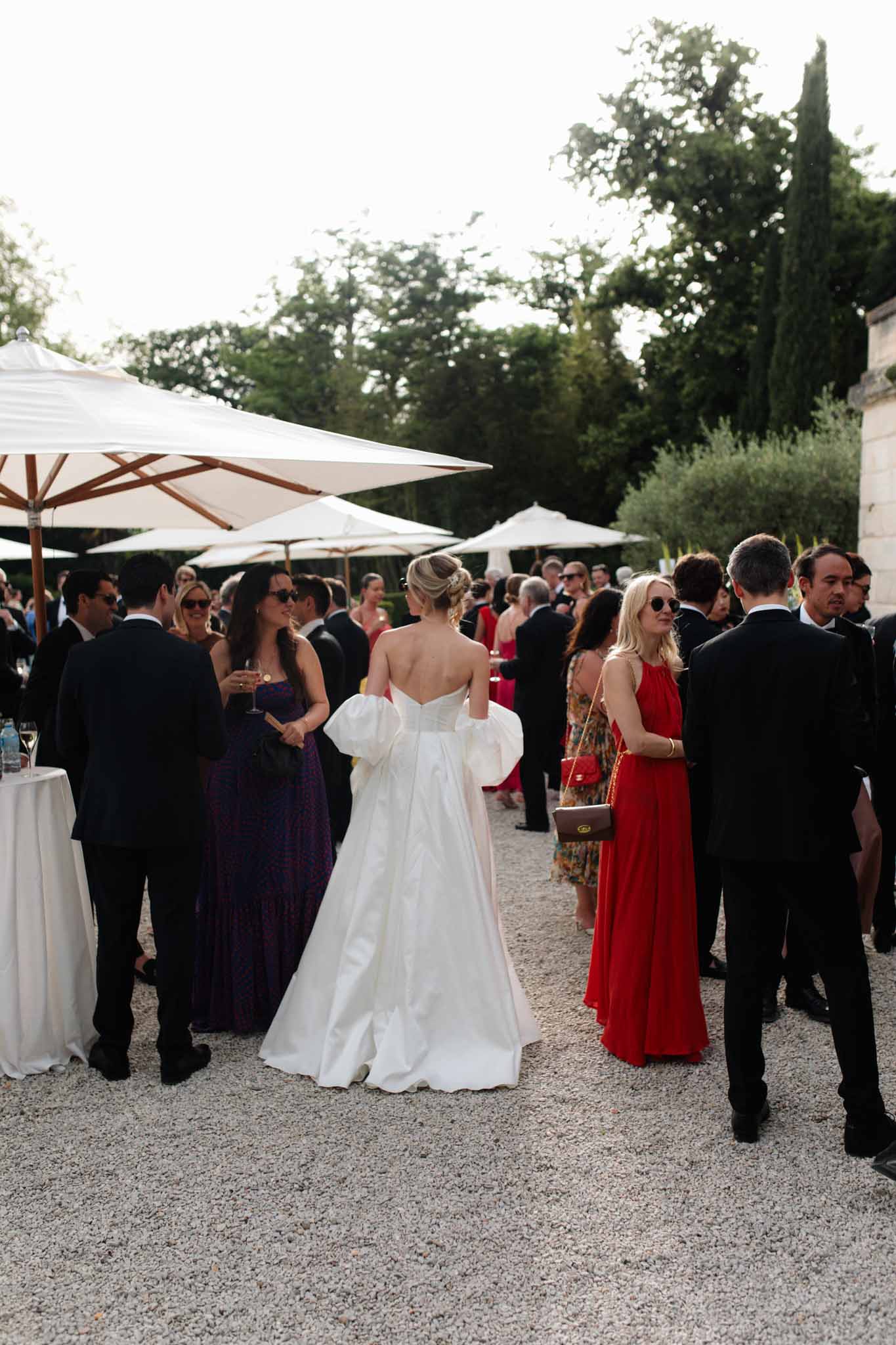 Bride in ivory ball gown with large back bow at outdoor cocktail hour under white umbrellas with guests behind