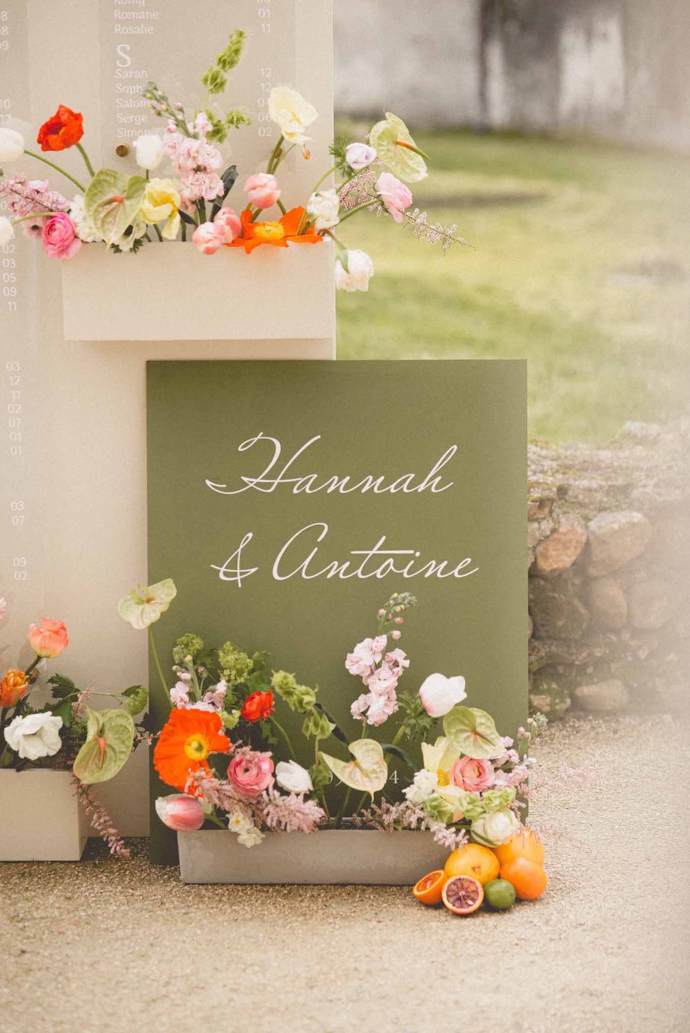 Wedding welcome sign reading Hannah and Antoine with orange poppies, pink ranunculus, and citrus fruit display