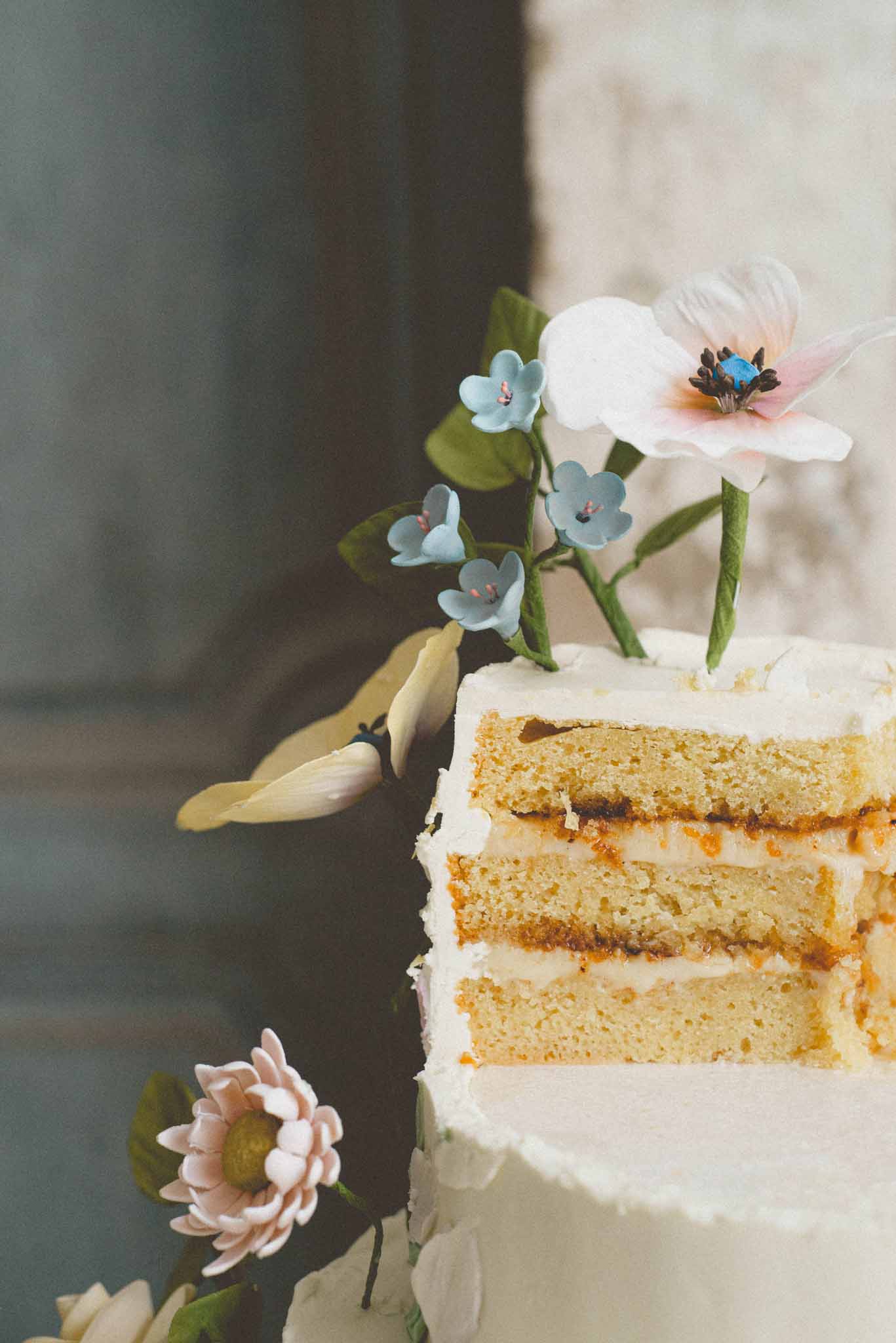 Sliced wedding cake showing yellow sponge layers with jam filling, decorated with handcrafted sugar flowers