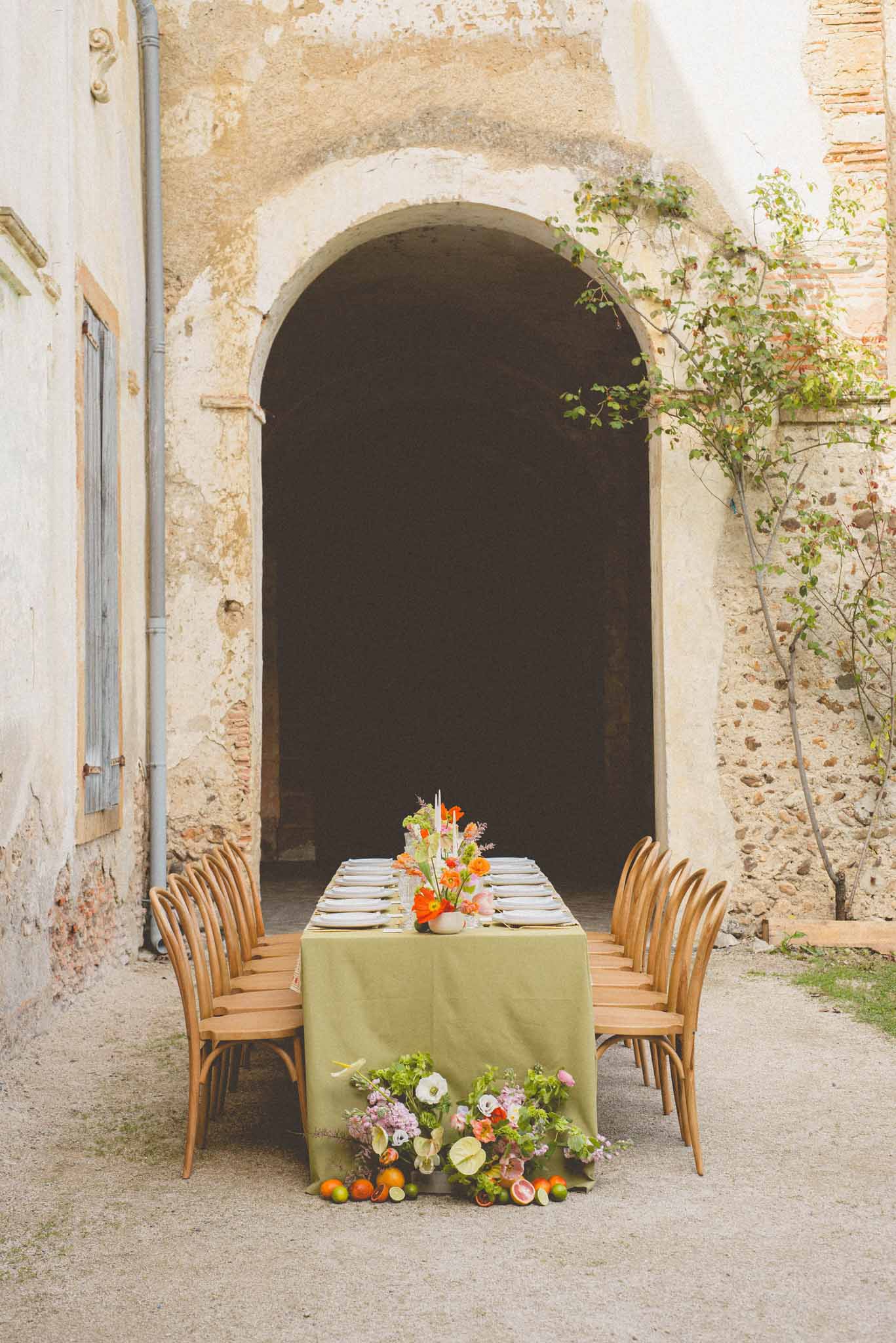 Olive linen table with orange poppy and lavender centerpiece and citrus floor display in stone courtyard