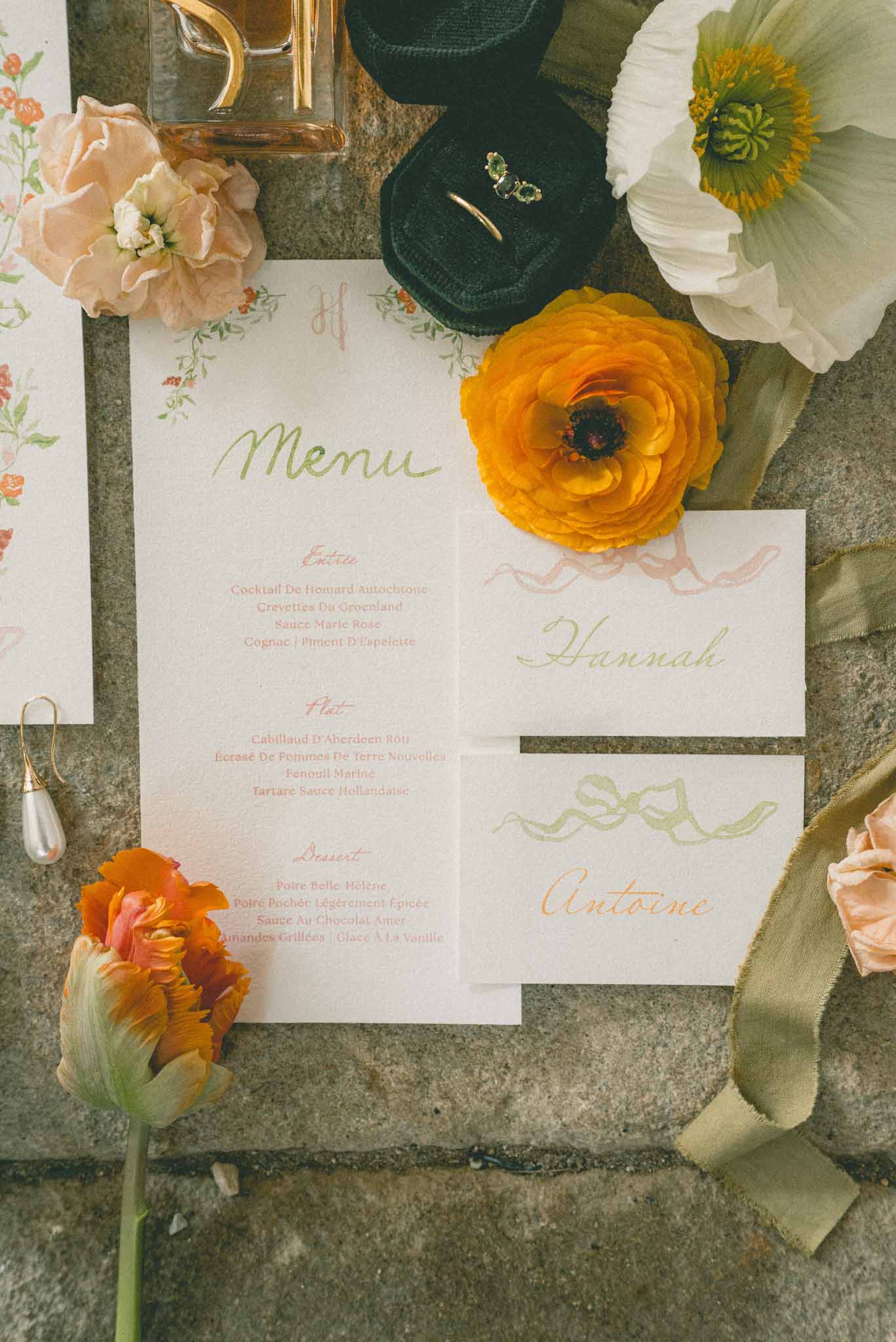 Flat lay of wedding stationery with calligraphy menu and place cards surrounded by ranunculus and silk ribbon
