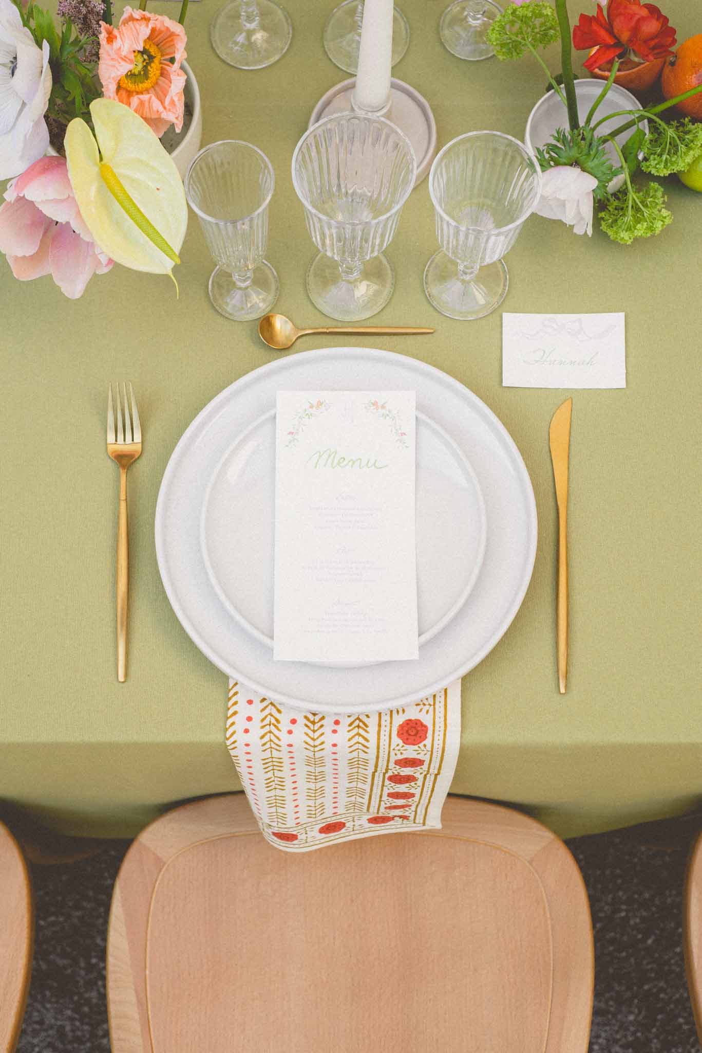 Overhead flat lay of reception place setting with gold cutlery, printed menu, and coral and pink floral arrangements