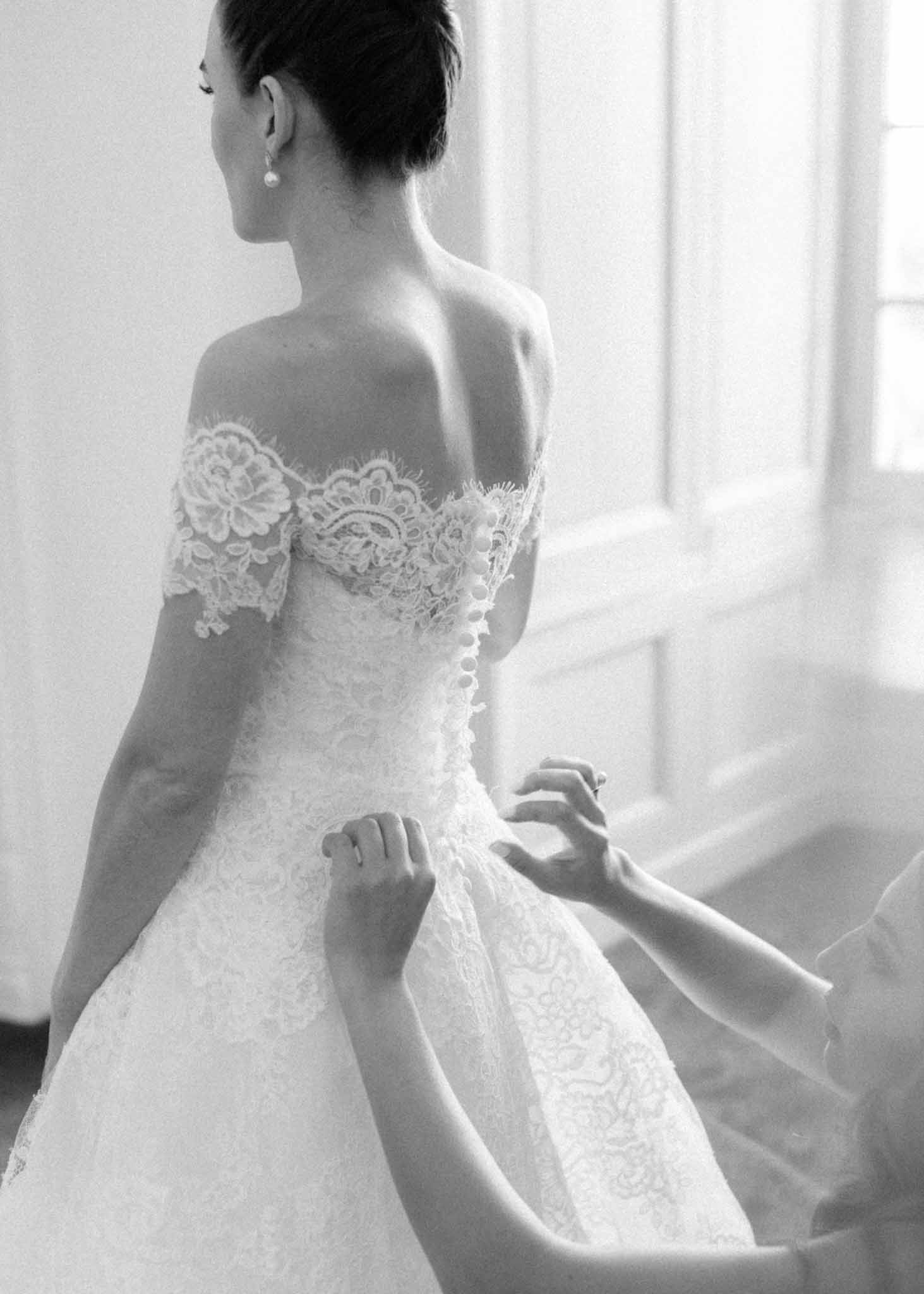 Back view of bride having strapless lace wedding gown fastened with pearl earrings and upswept hair in black and white