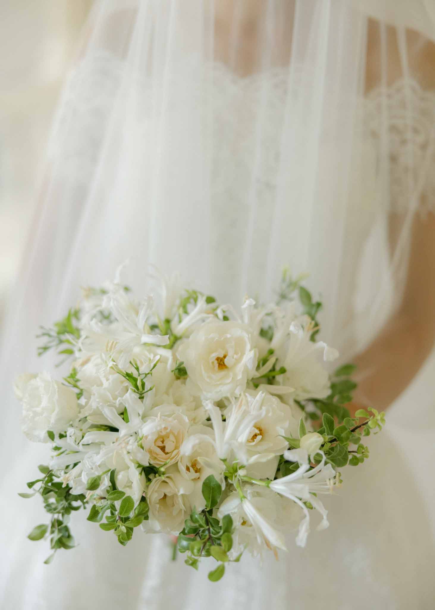 Close-up of bridal bouquet with cream garden roses, white jasmine, and eucalyptus held against an ivory gown and veil