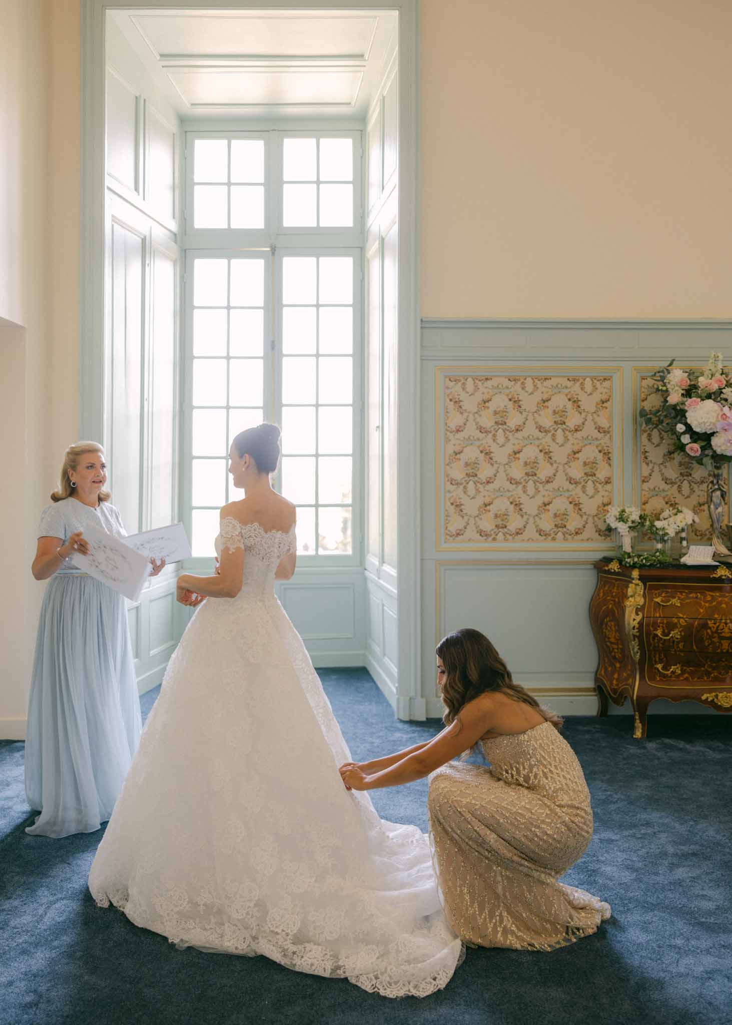 Bridesmaid helping bride fix and adjust her wedding dress while getting ready at Saint-Martin