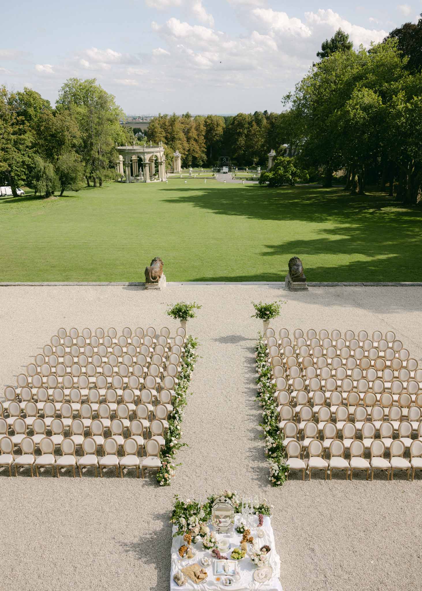 Aerial view of outdoor ceremony setup with wooden chairs on a paved terrace leading to a neoclassical stone pavilion