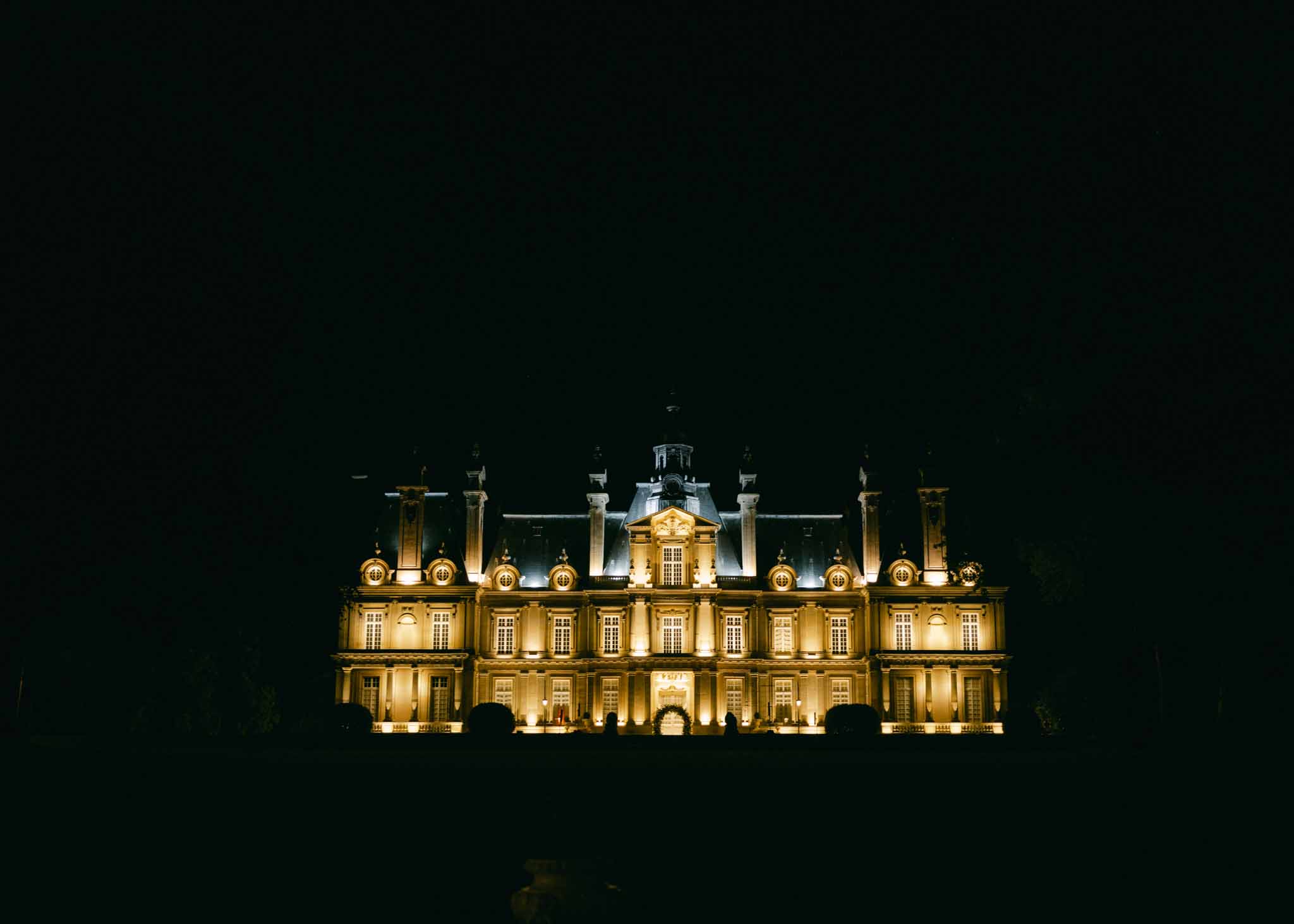 Grand chateau facade illuminated with warm golden uplighting against a dark night sky with central cupola
