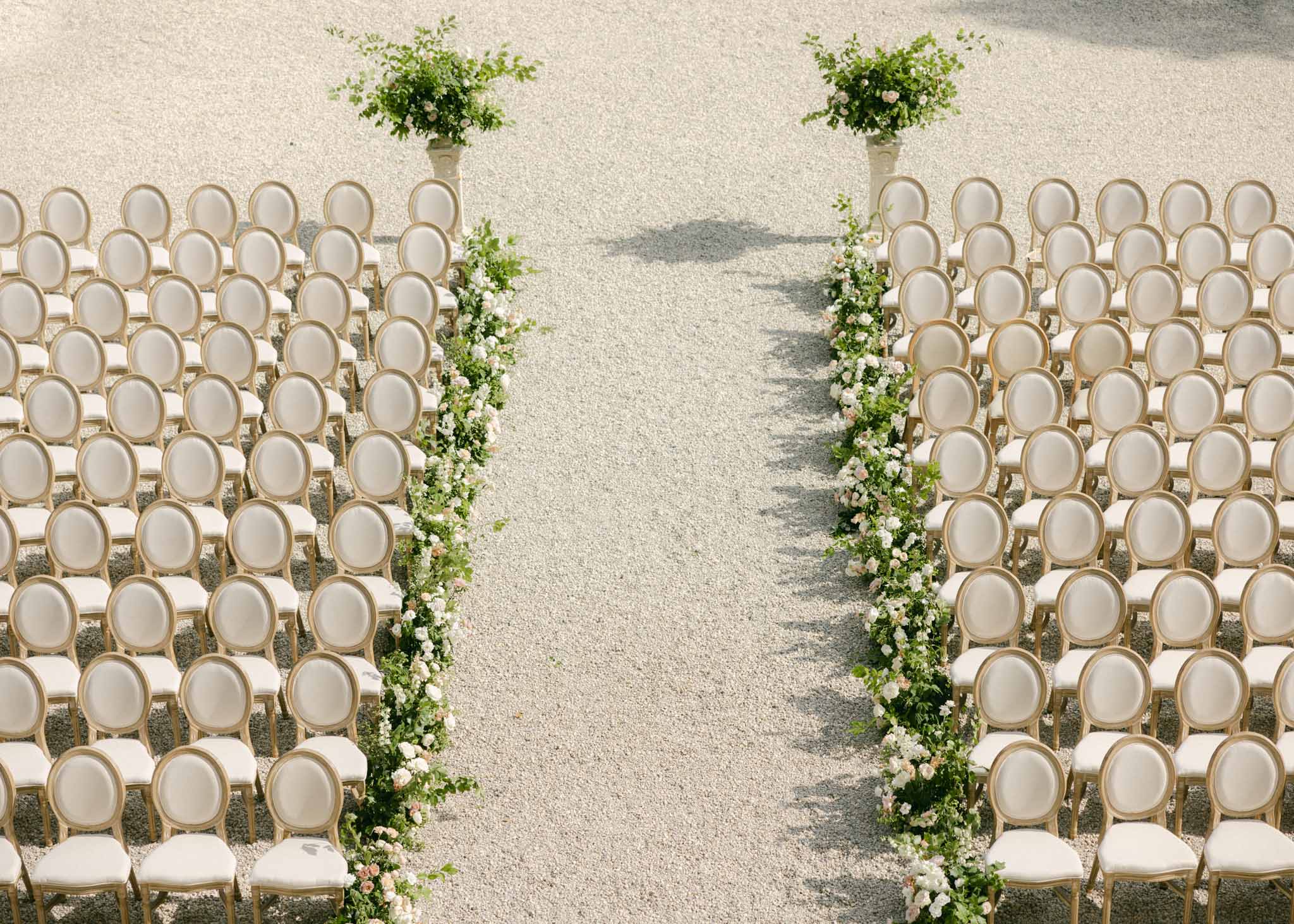 Overhead view of outdoor ceremony seating with wood chairs, ivy aisle borders, and white floral planters
