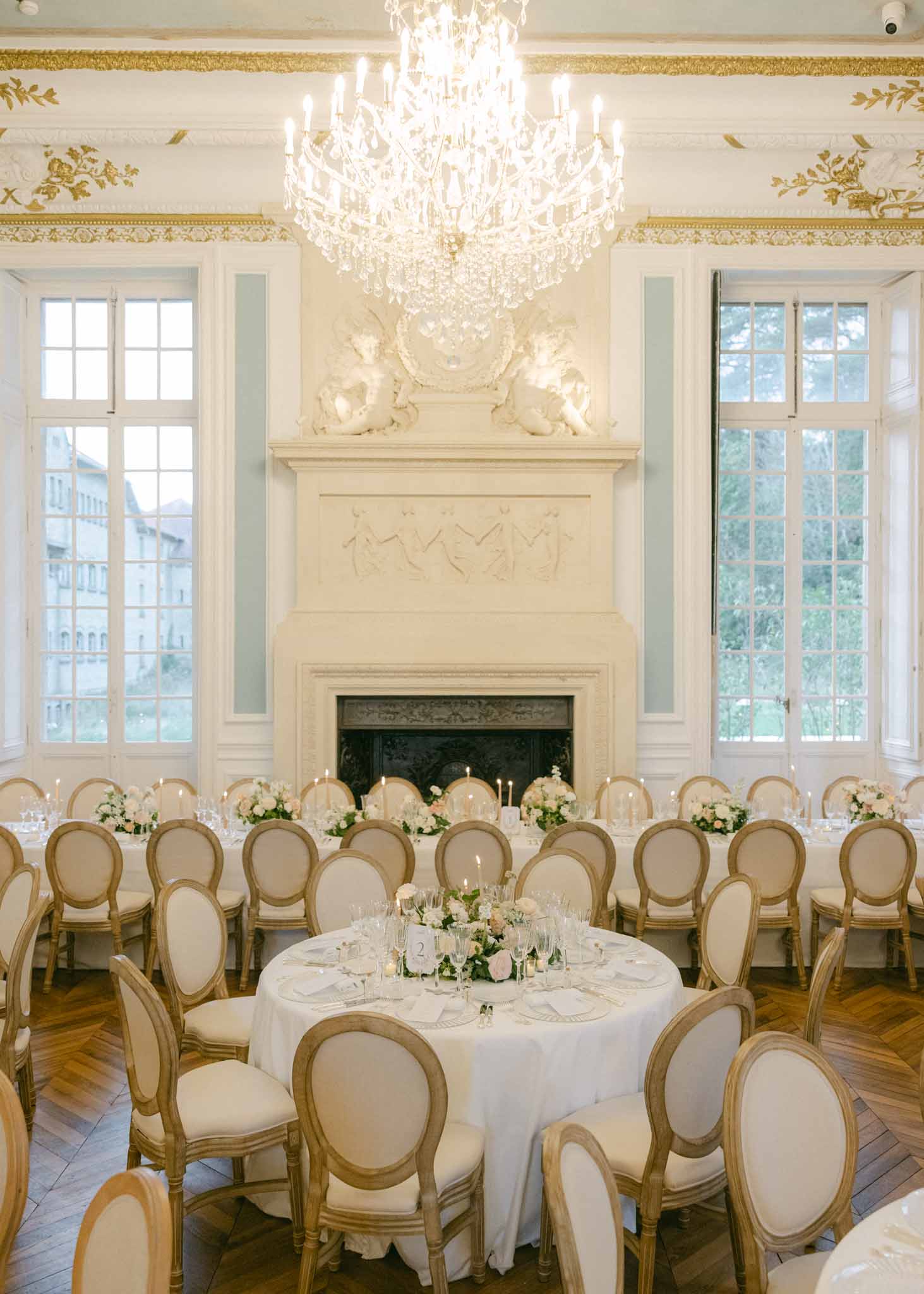 Round tables and chairs set for reception under glass chandelier at Chateau Saint-Martin by H Clark