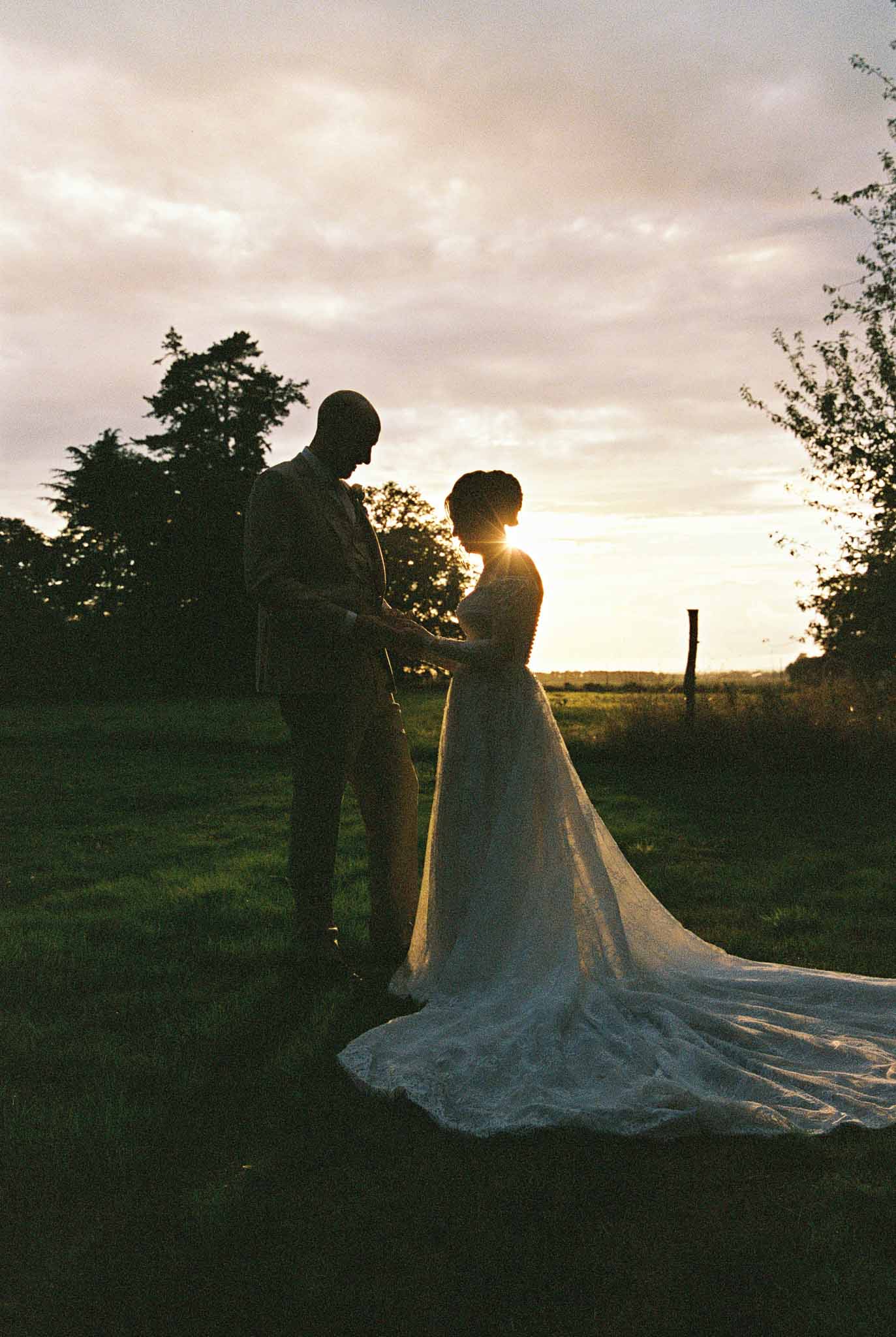 Bride and groom holding hands in countryside field during golden hour portrait session