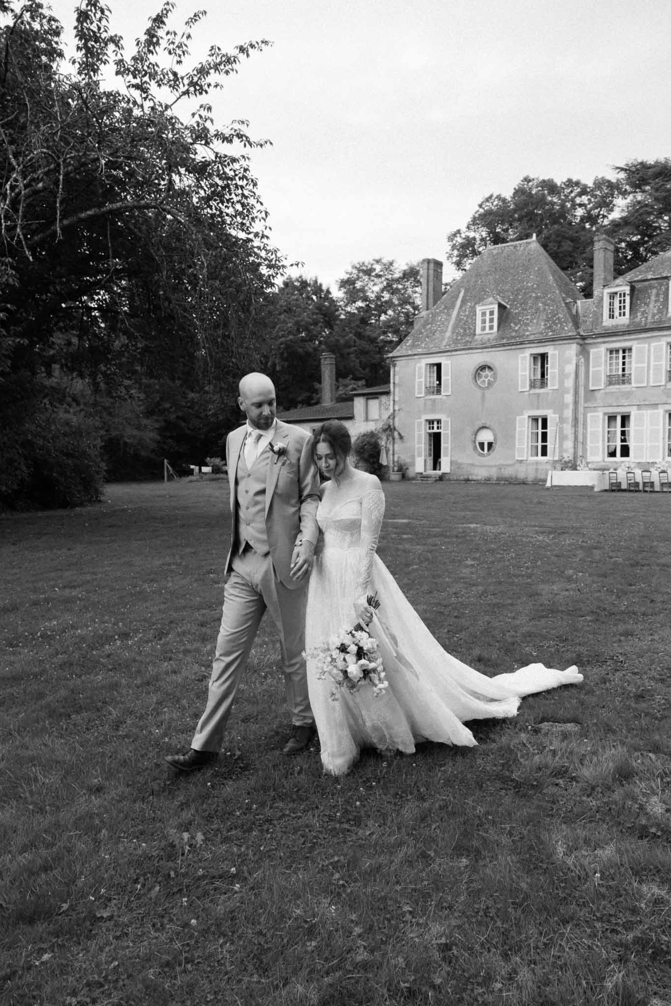 Wedding couple walking on chÃƒÂ¢teau lawn in black and white portrait
