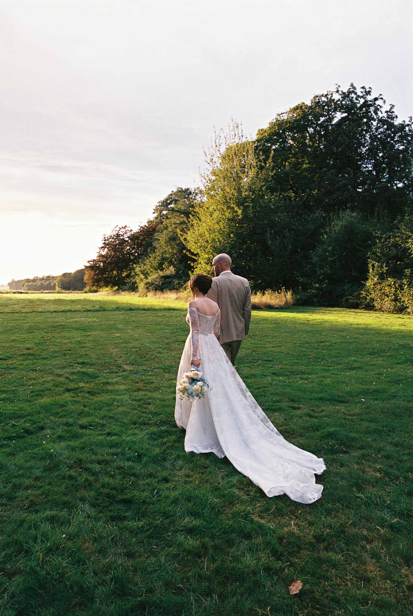 Bride and groom walking together across grassy field during golden hour wedding photography
