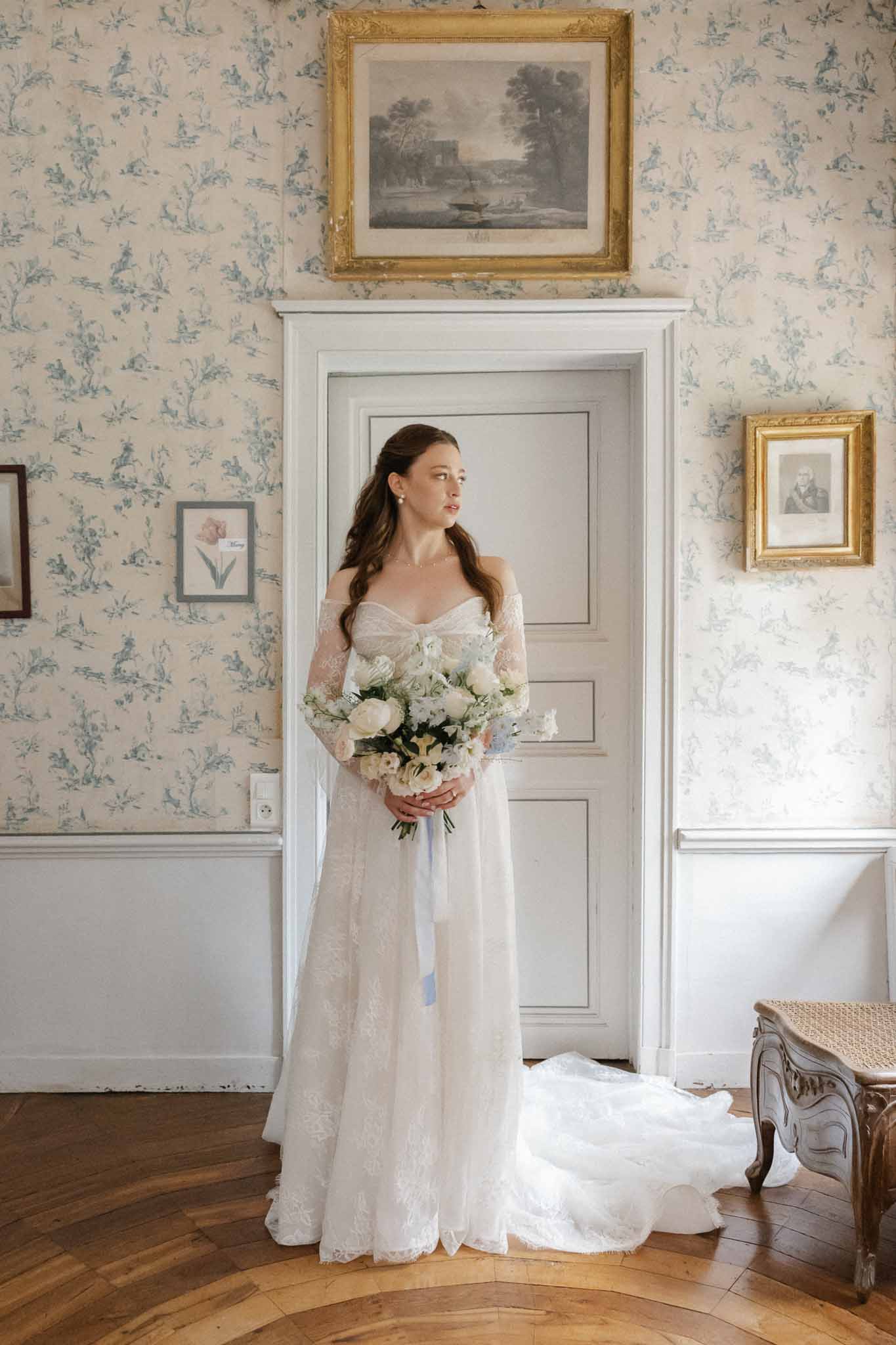 Bride in ivory lace gown holding bouquet in elegant French-inspired interior room