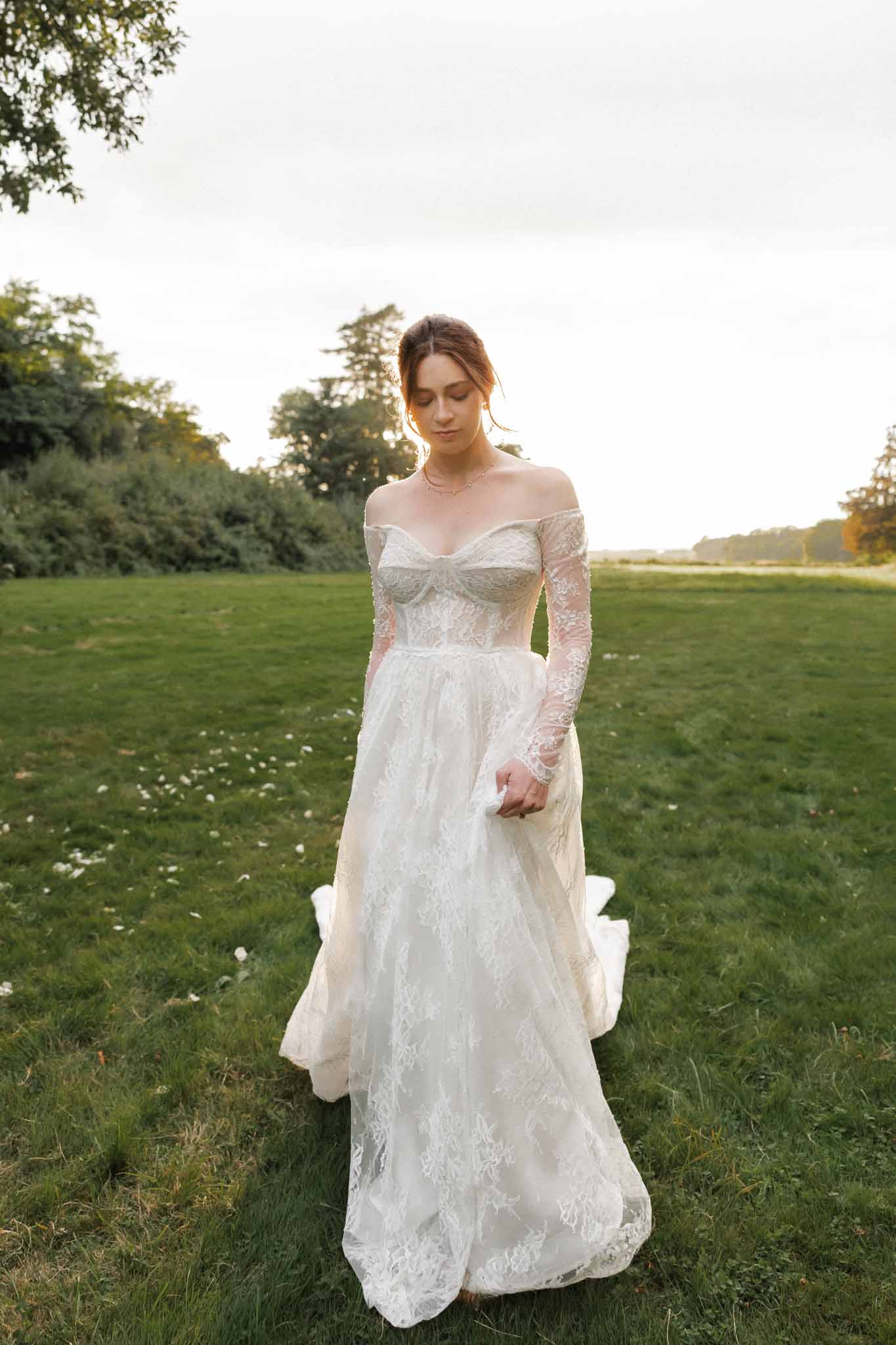 Bride in ivory lace wedding dress standing in open field with trees