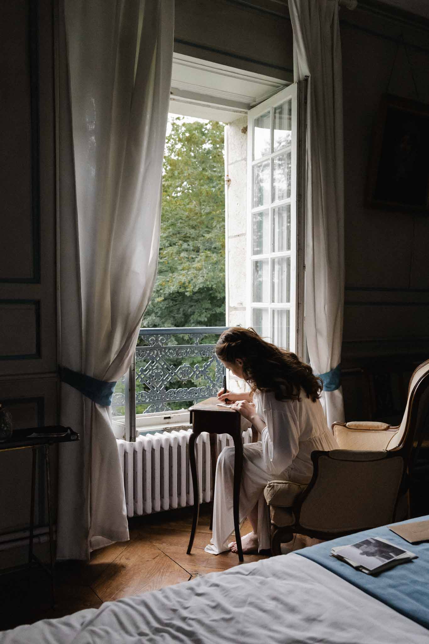 Bride writing at desk near French doors in historic chÃƒÂ¢teau interior room