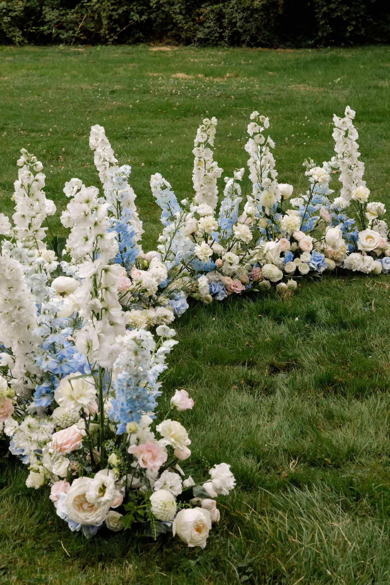 Row of pastel floral arrangements lining outdoor wedding ceremony lawn with white and blush blooms