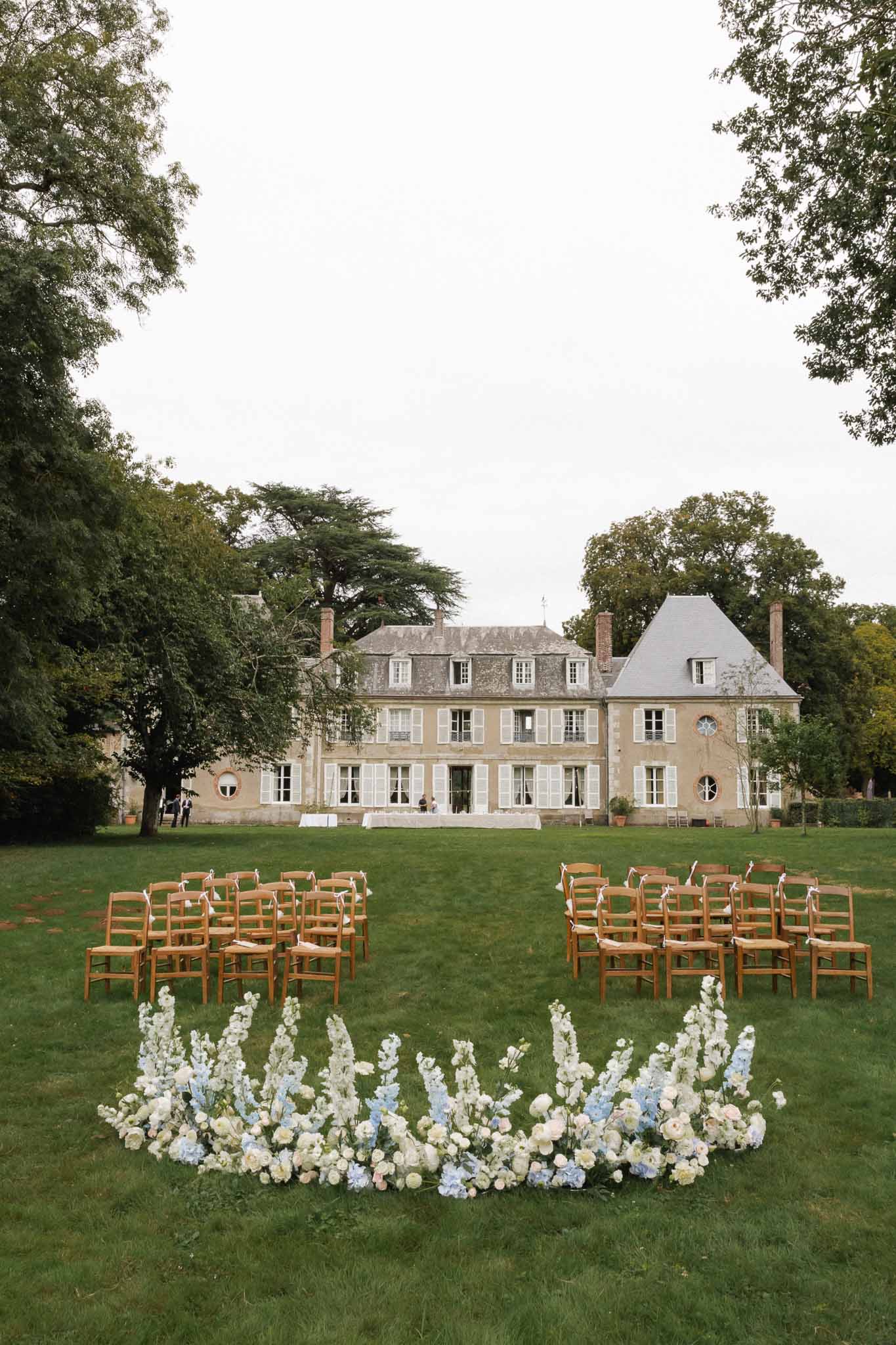 Outdoor wedding ceremony setup on chÃƒÂ¢teau lawn with floral installation and neoclassical French mansion backdrop
