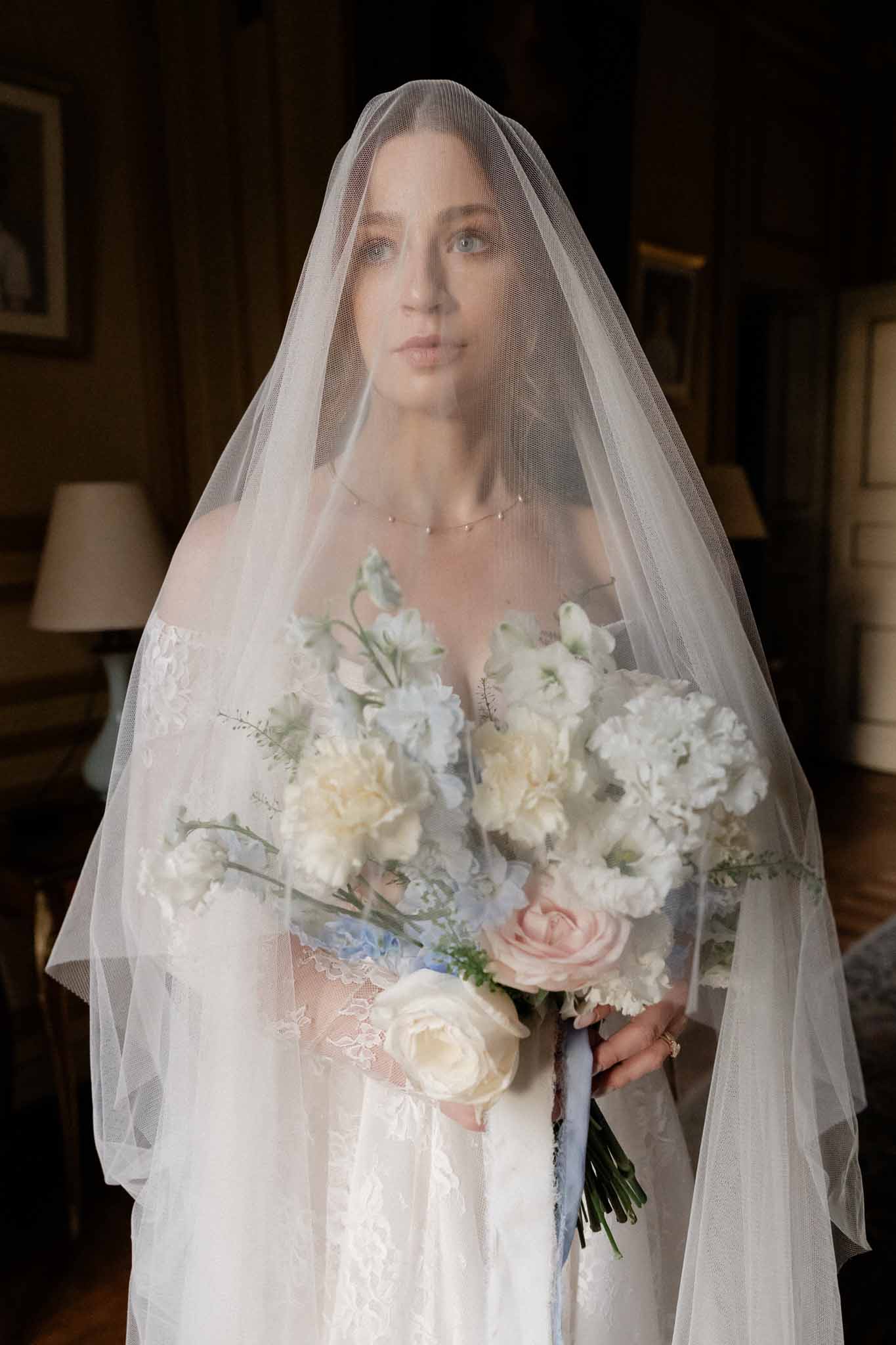 Bride in ivory lace wedding dress with bouquet in elegant interior setting