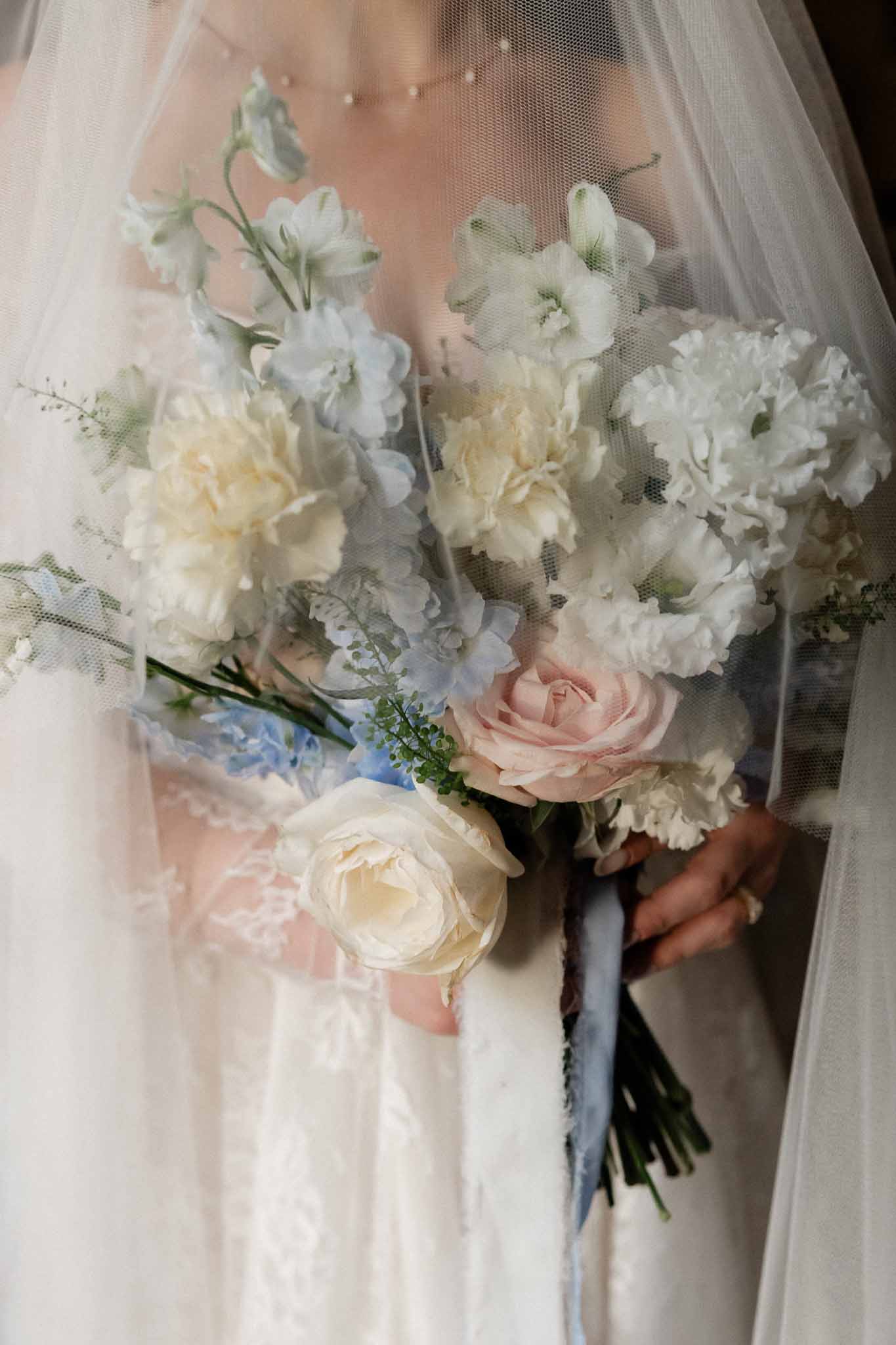Bride holding ivory and blush bouquet against lace wedding dress with blue silk ribbon
