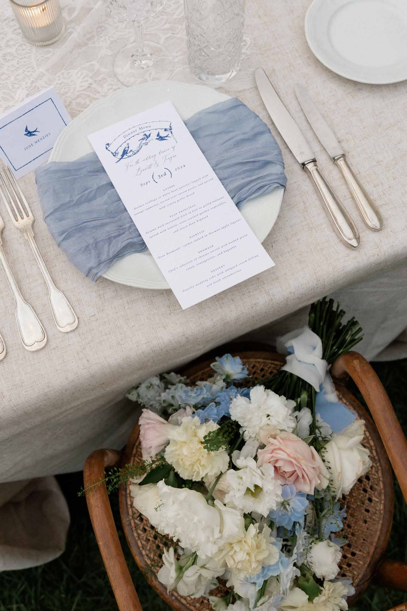 Blue and white wedding table setting with menu cards and bridal bouquet at reception venue