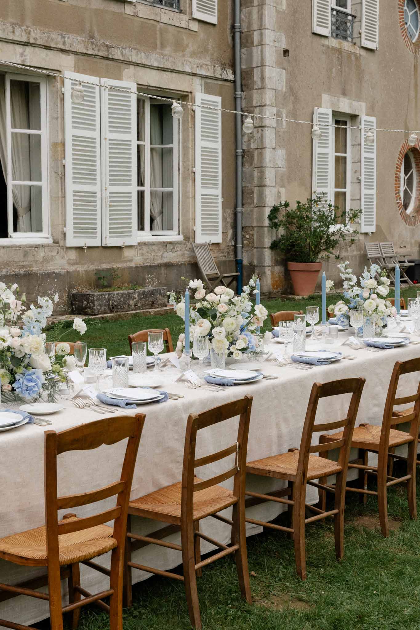 Long banquet table with white linens and blue accents set in European courtyard for wedding reception