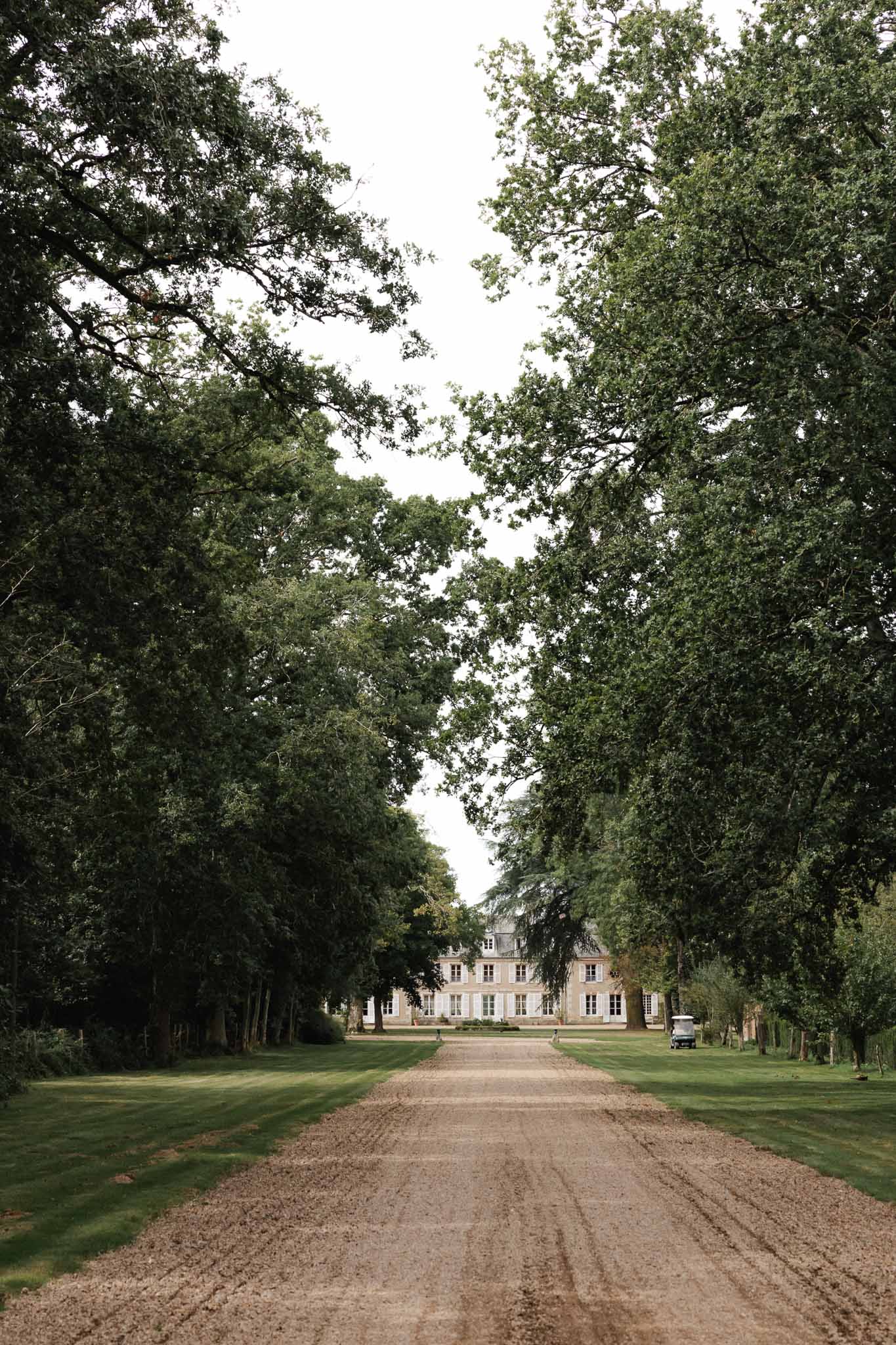 Tree-lined driveway leading to classical stone chÃƒÂ¢teau wedding venue with manicured grounds