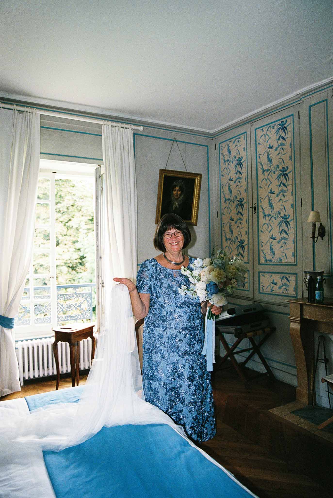 Woman in blue dress holding bridal bouquet in elegant chÃƒÂ¢teau bedroom with teal paneled walls