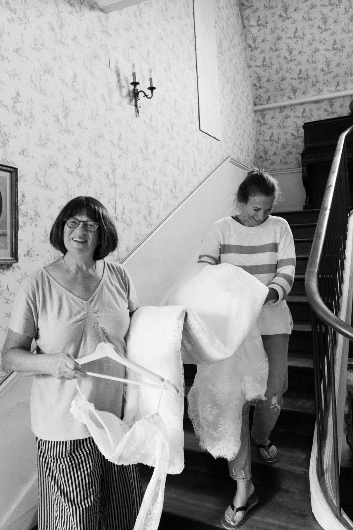 Two people handling wedding dress on staircase in period interior with floral wallpaper