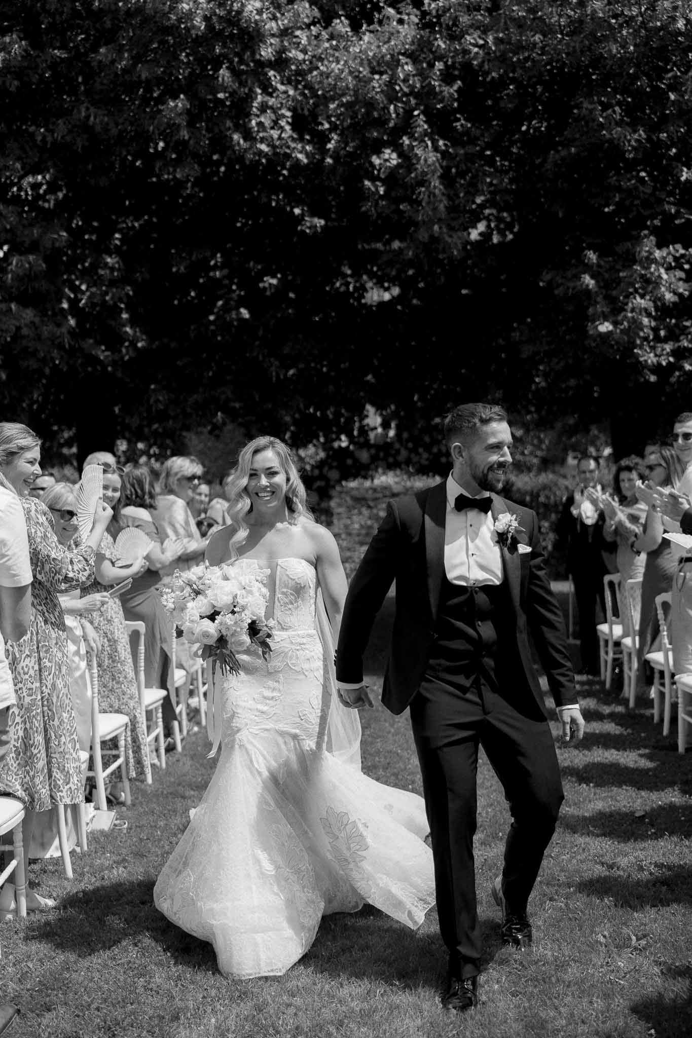 Newlywed couple walking down outdoor aisle after ceremony with guests applauding in garden setting