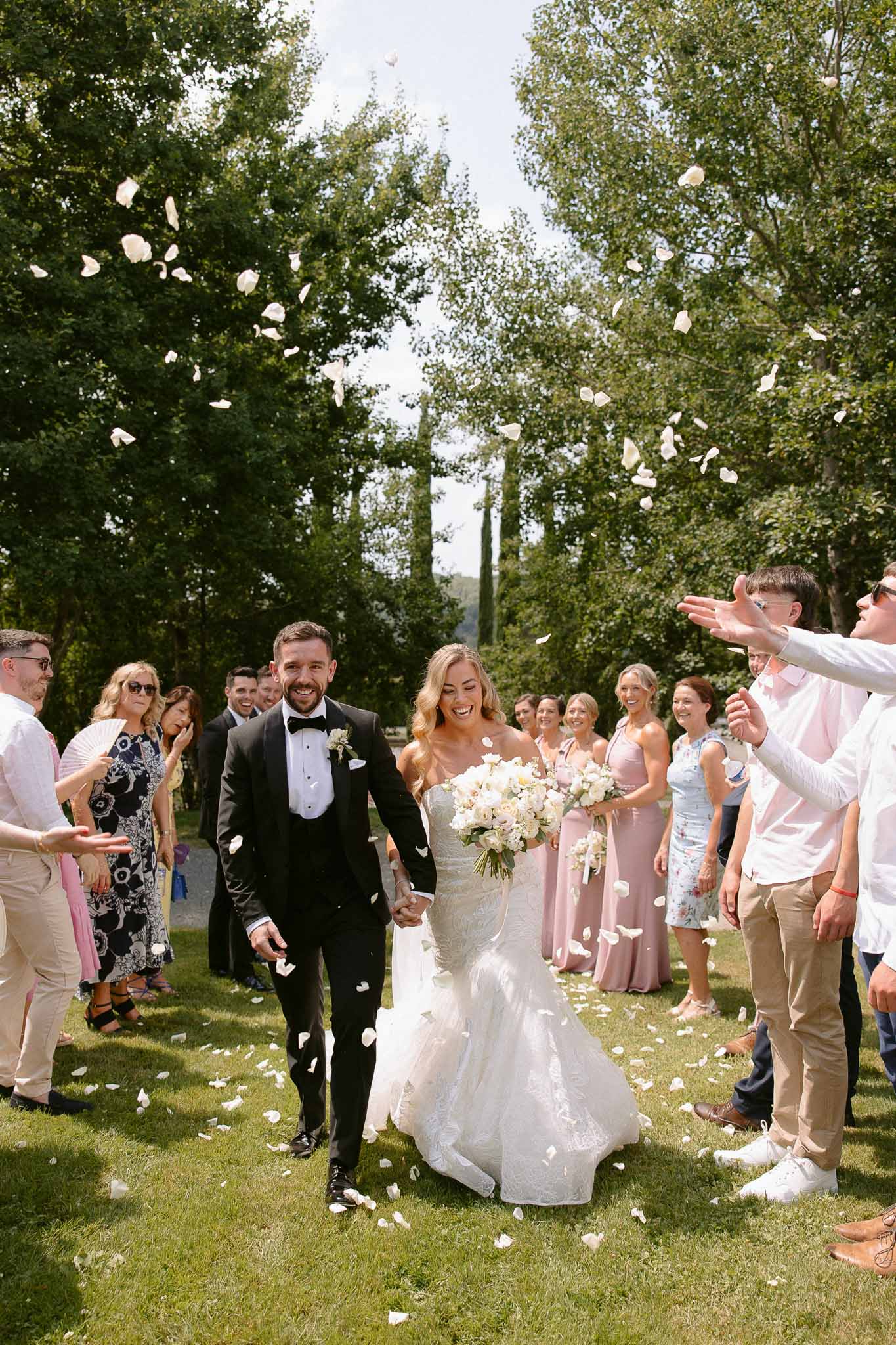 Couple walking down outdoor aisle during recessional with guests tossing petals in garden ceremony