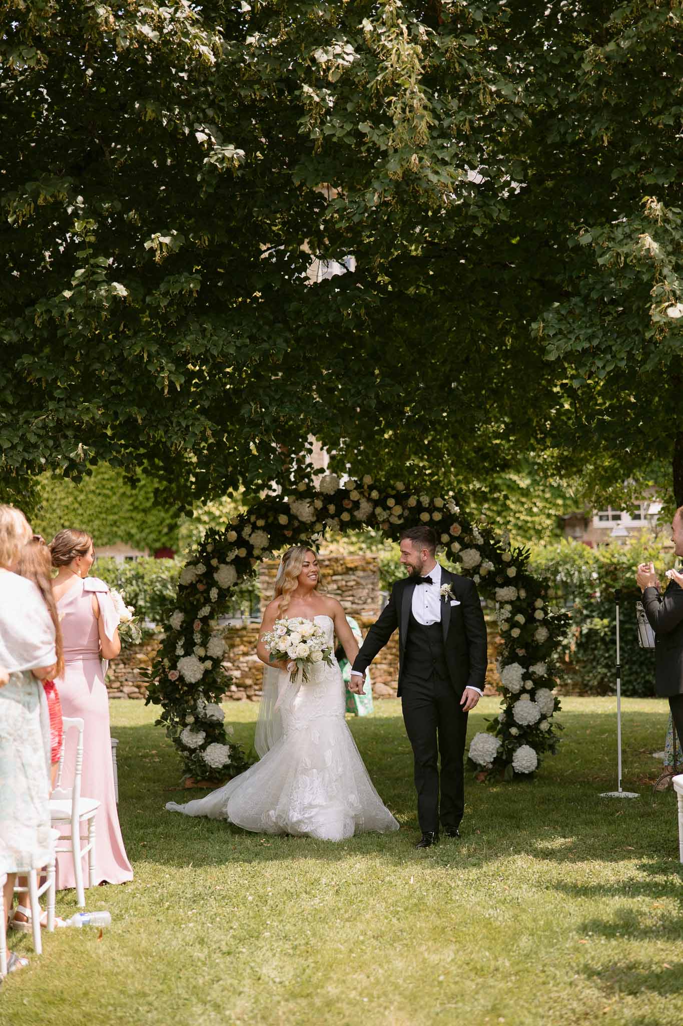 Bride and groom walking down aisle during outdoor garden ceremony with black altar and white hydrangea arrangements