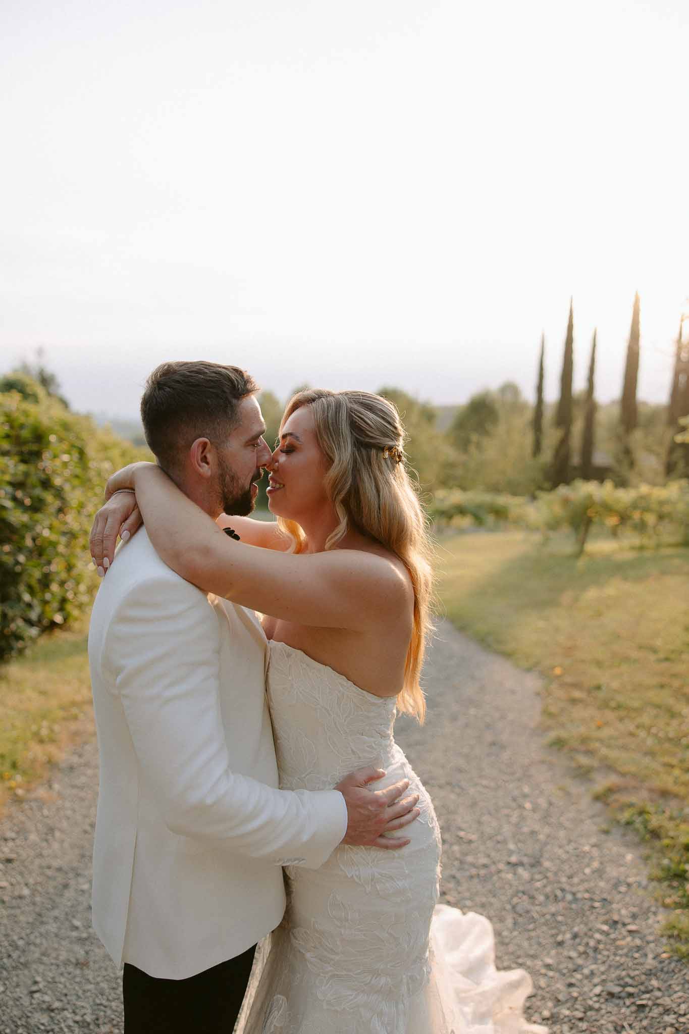 Bride and groom embracing on tree-lined pathway at vineyard wedding venue during golden hour