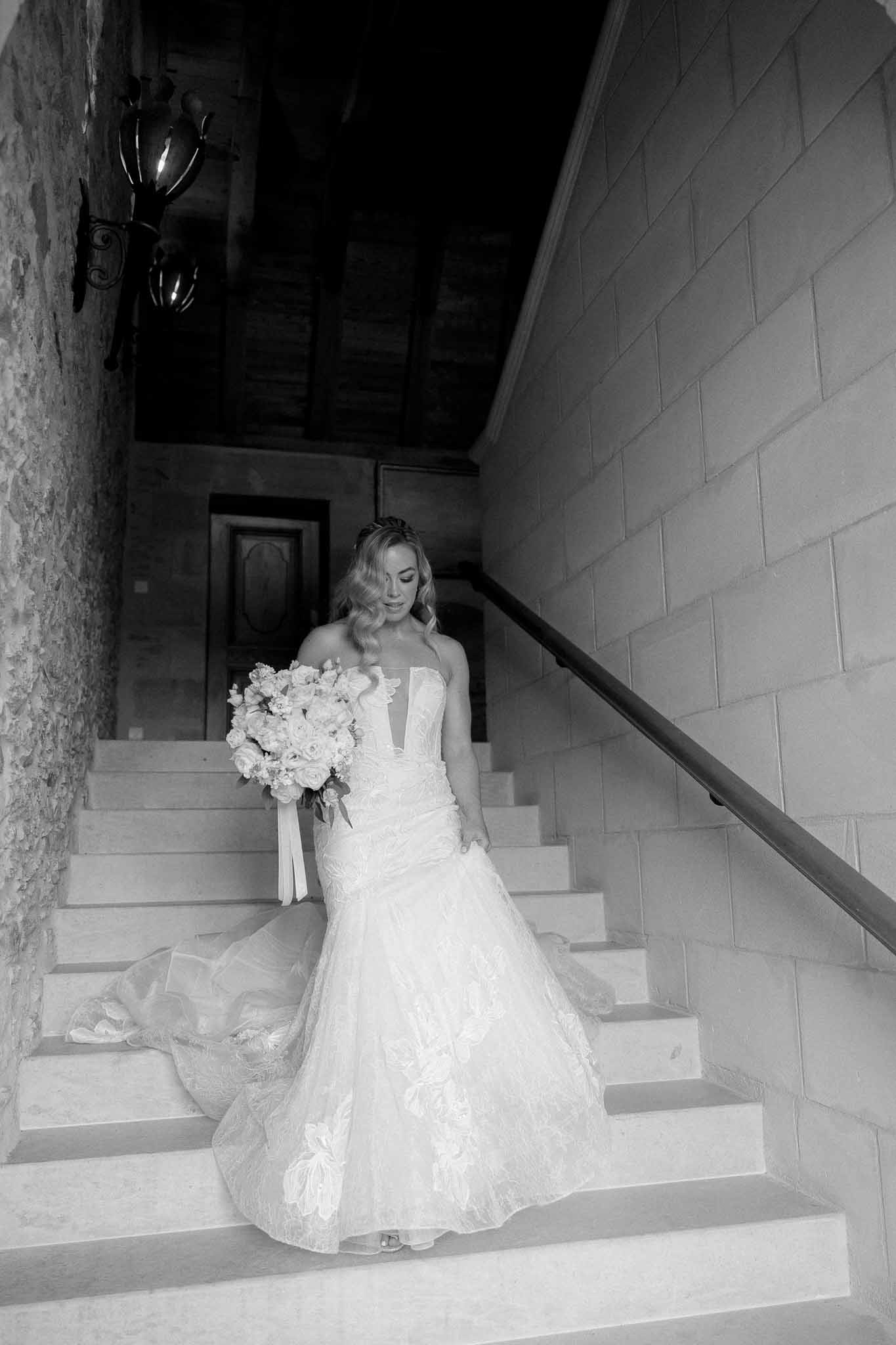 Bride in mermaid gown descending stone staircase in modern architectural venue