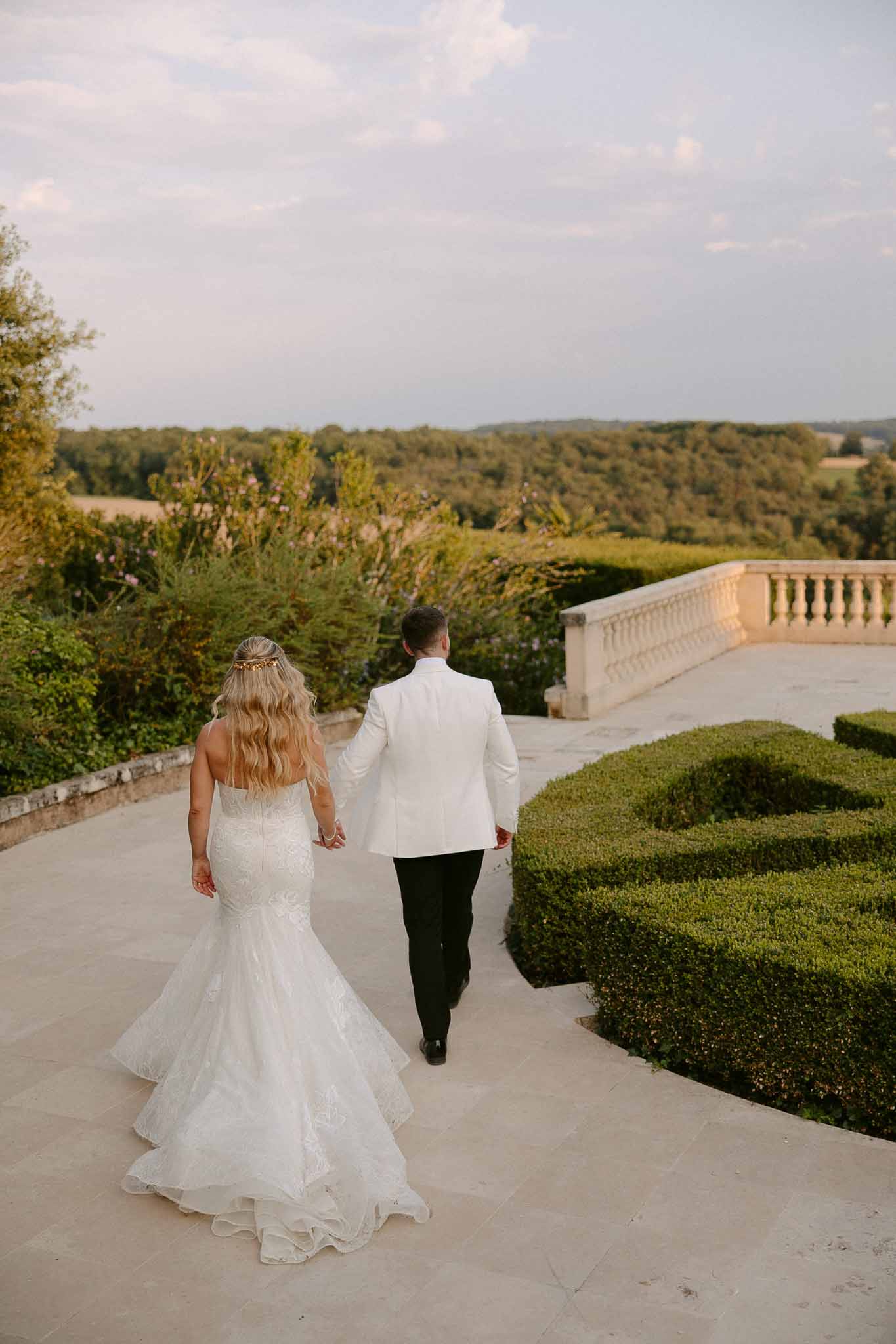 Bride and groom walking on stone terrace overlooking forested landscape at chÃƒÂ¢teau estate