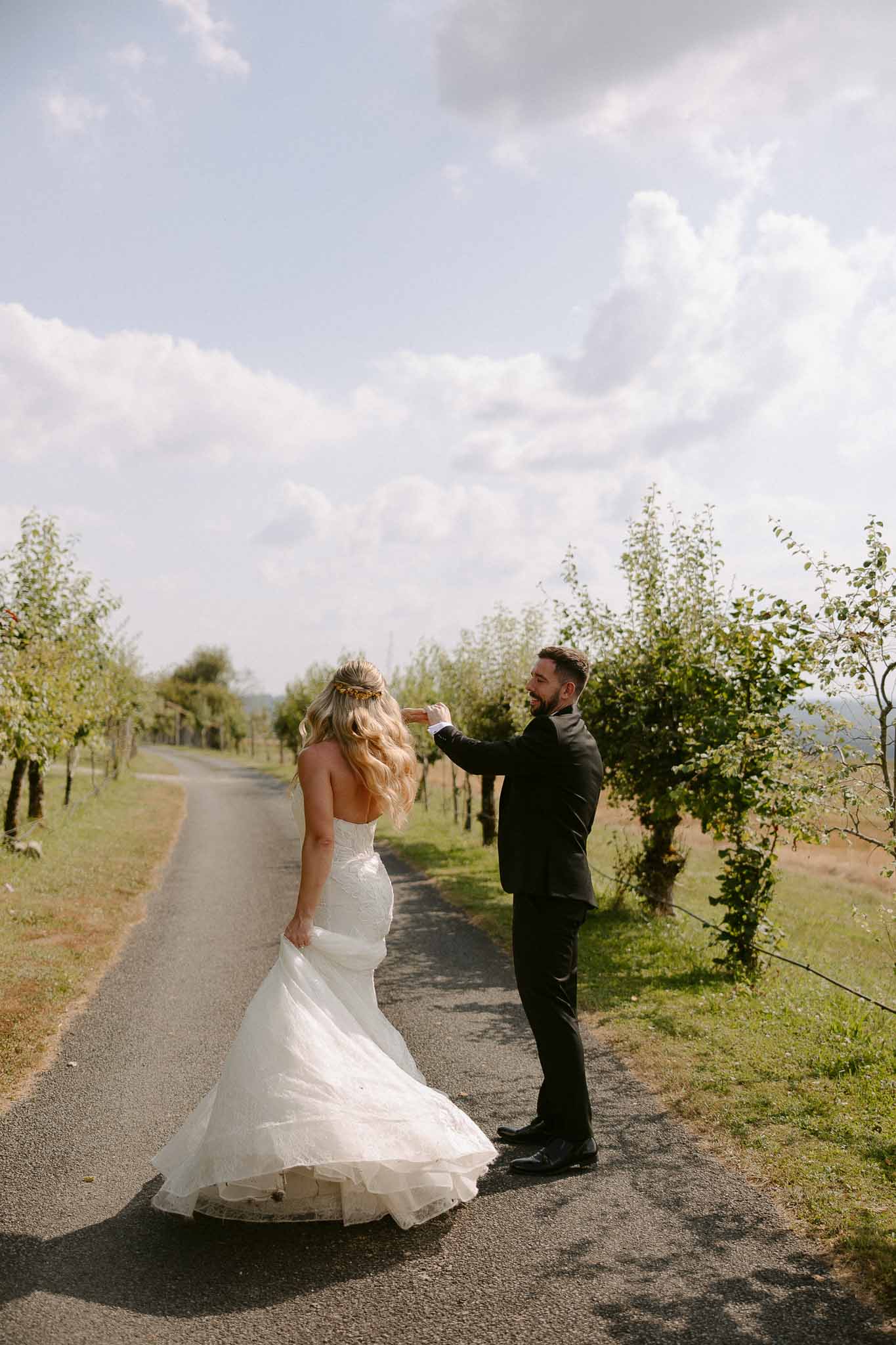 Bride and groom portrait on tree-lined vineyard lane with groom adjusting bride's hair