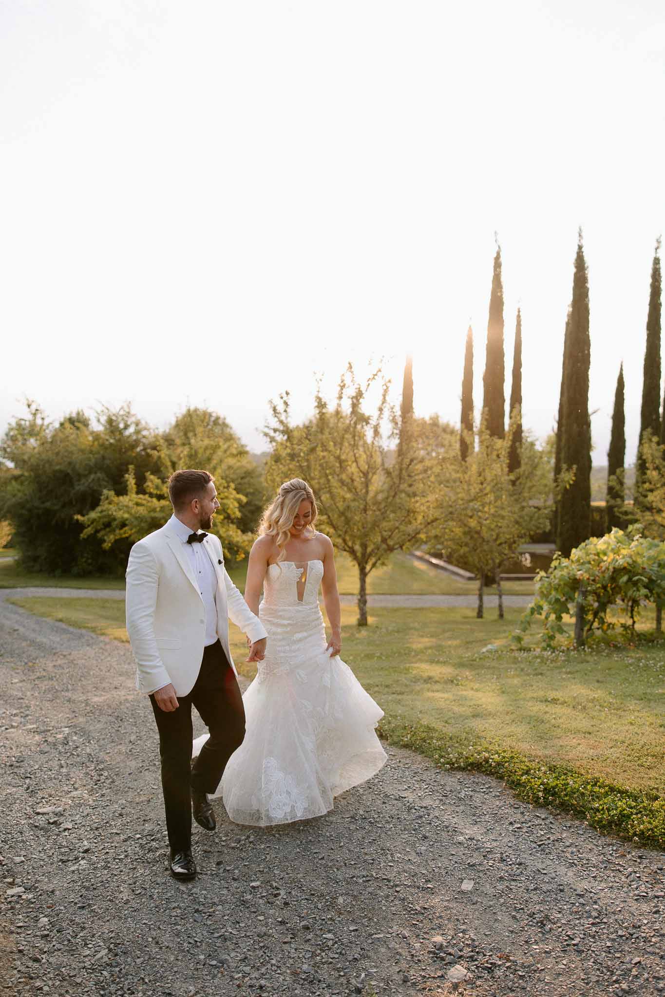 Bride and groom walking hand-in-hand through Mediterranean garden with cypress trees