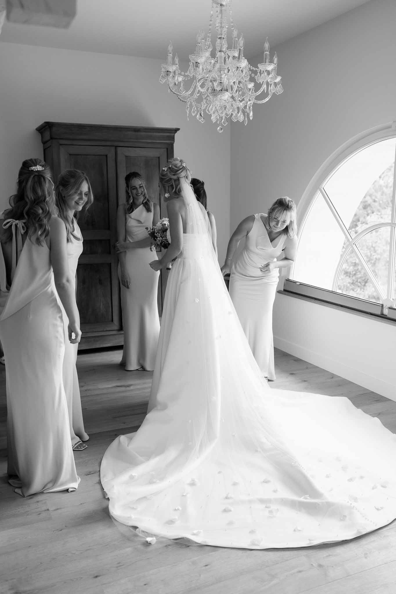 Bride with bridesmaids getting ready in elegant indoor room with crystal chandelier