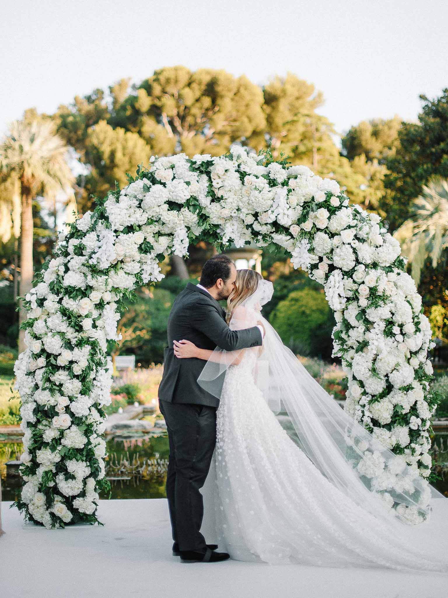 Bride and groom kissing under floral arch during outdoor garden wedding ceremony