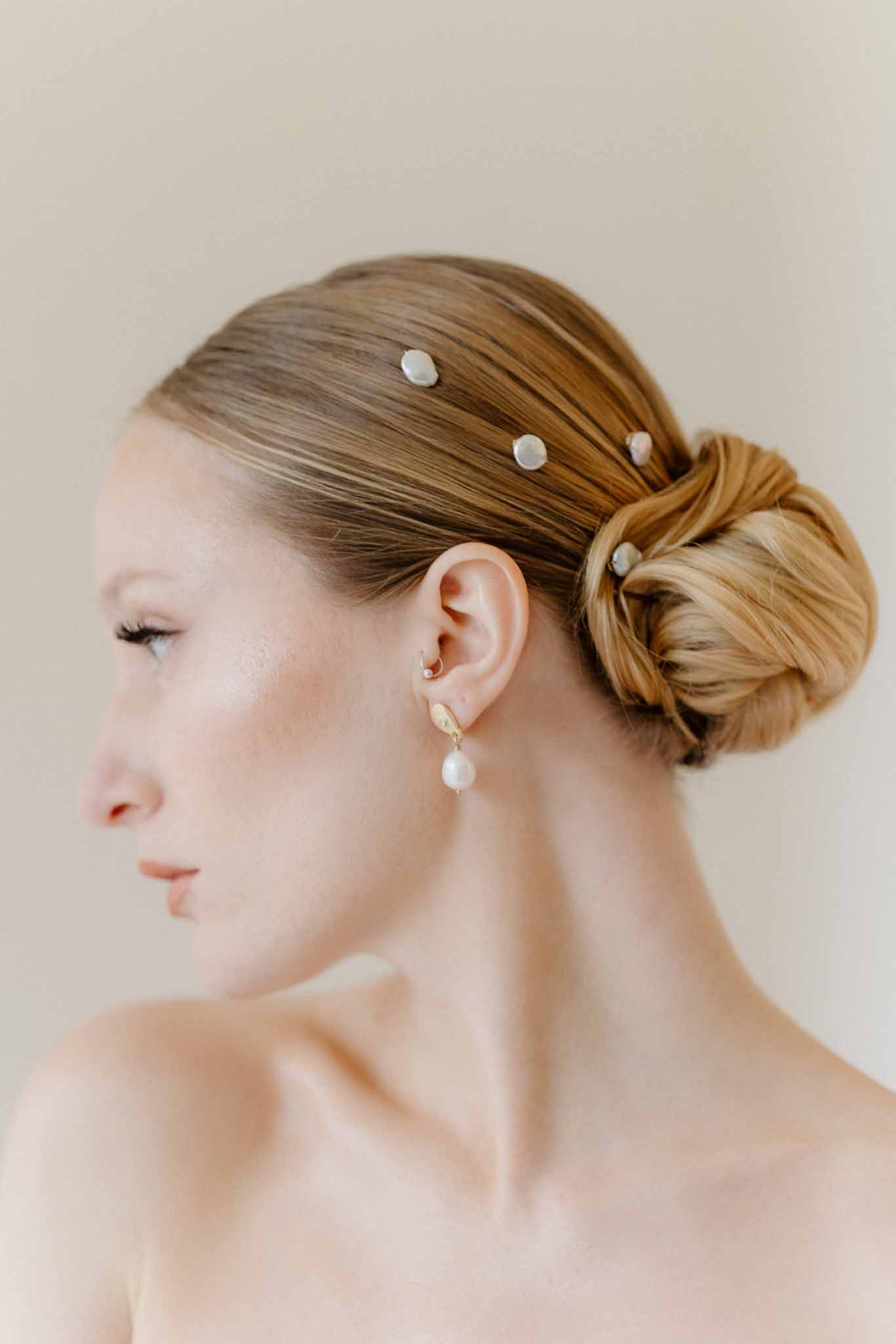 Bride profile portrait showing pearl hair pins and drop earrings against neutral background