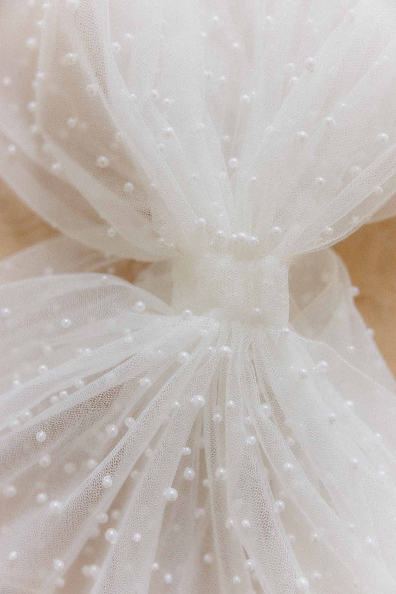 Close-up of ivory tulle wedding dress fabric with pearl bead embellishments