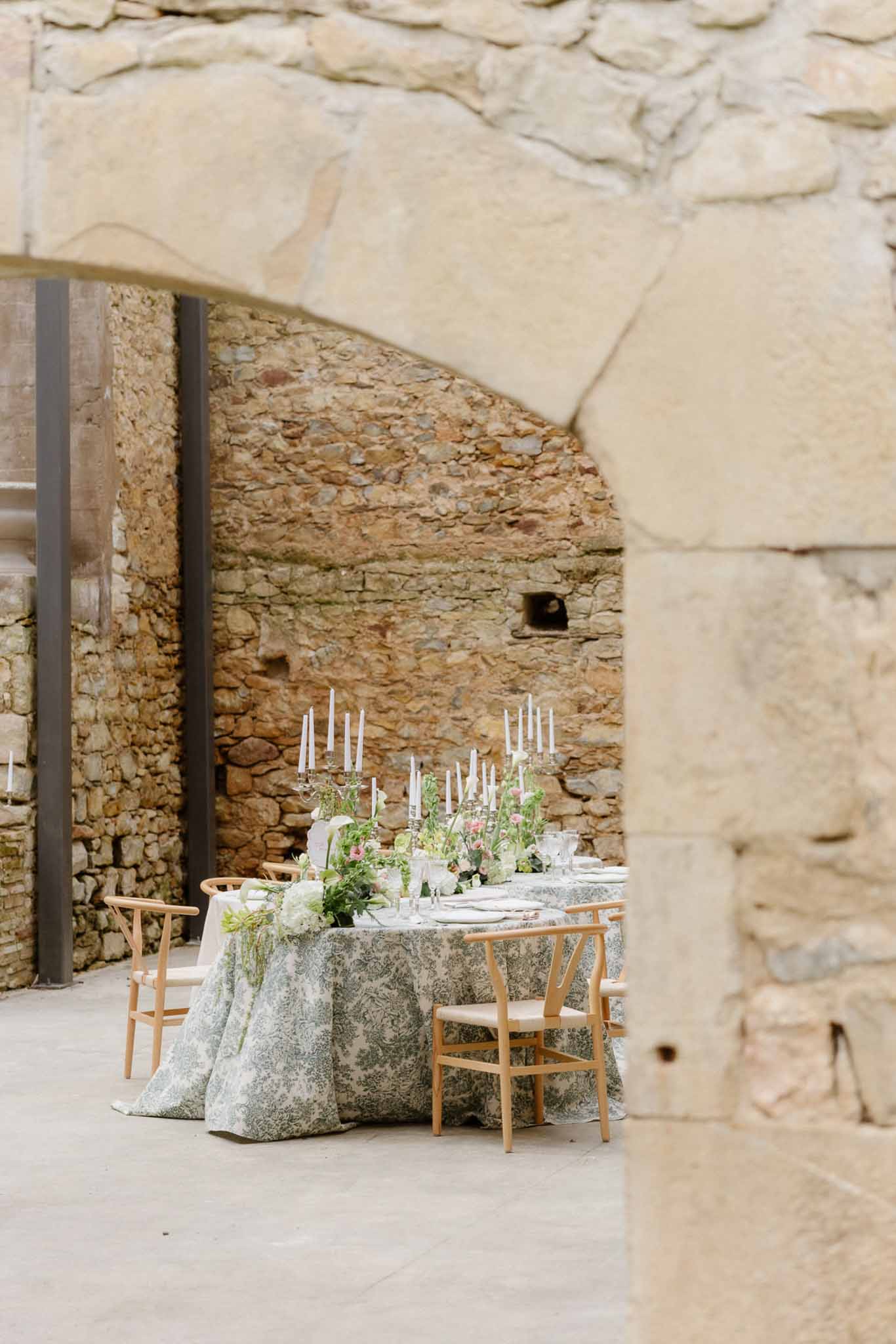 Reception table with sage linens and white flowers set in stone archway at historic venue