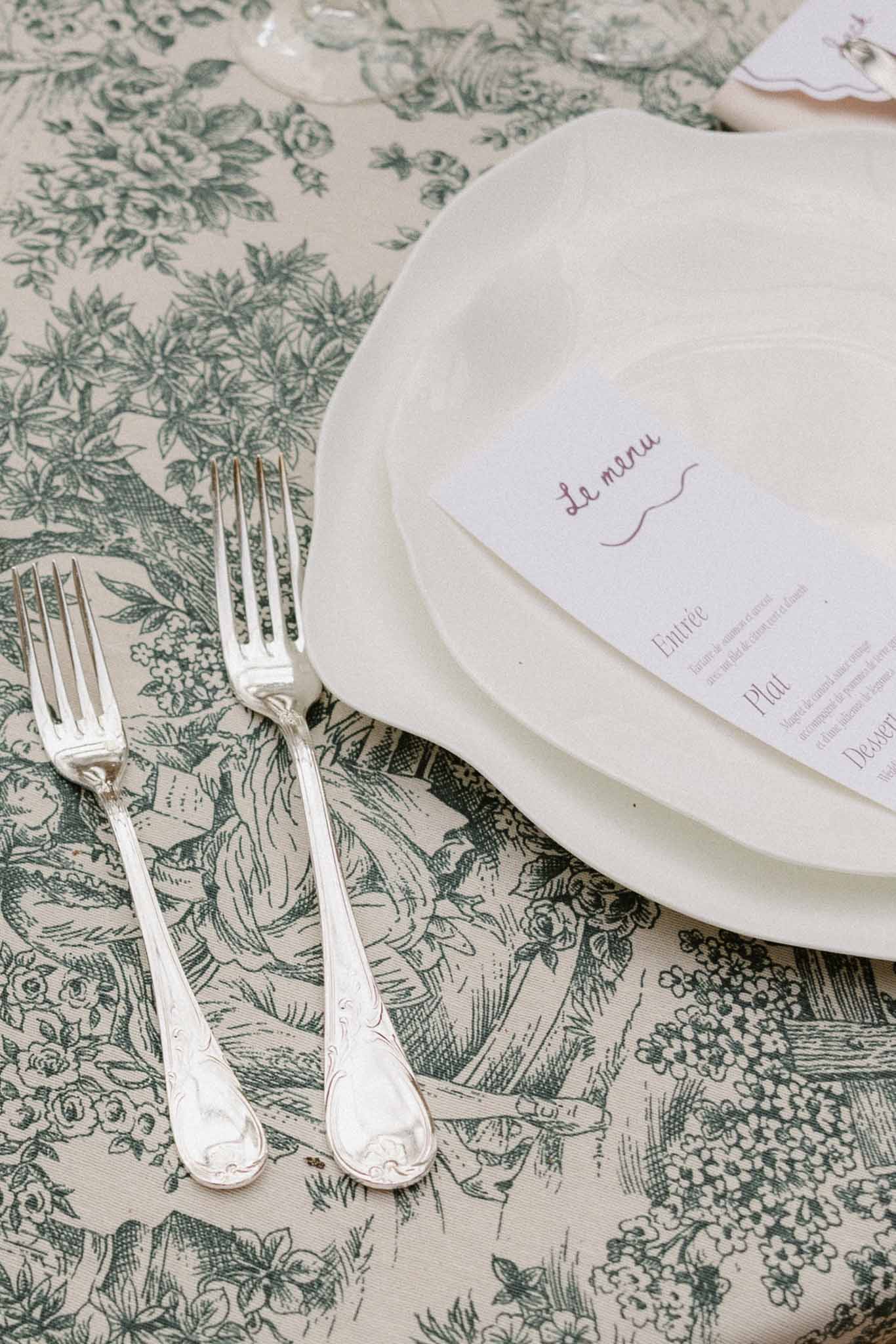 Elegant table place setting with botanical toile tablecloth and handwritten menu cards at wedding reception