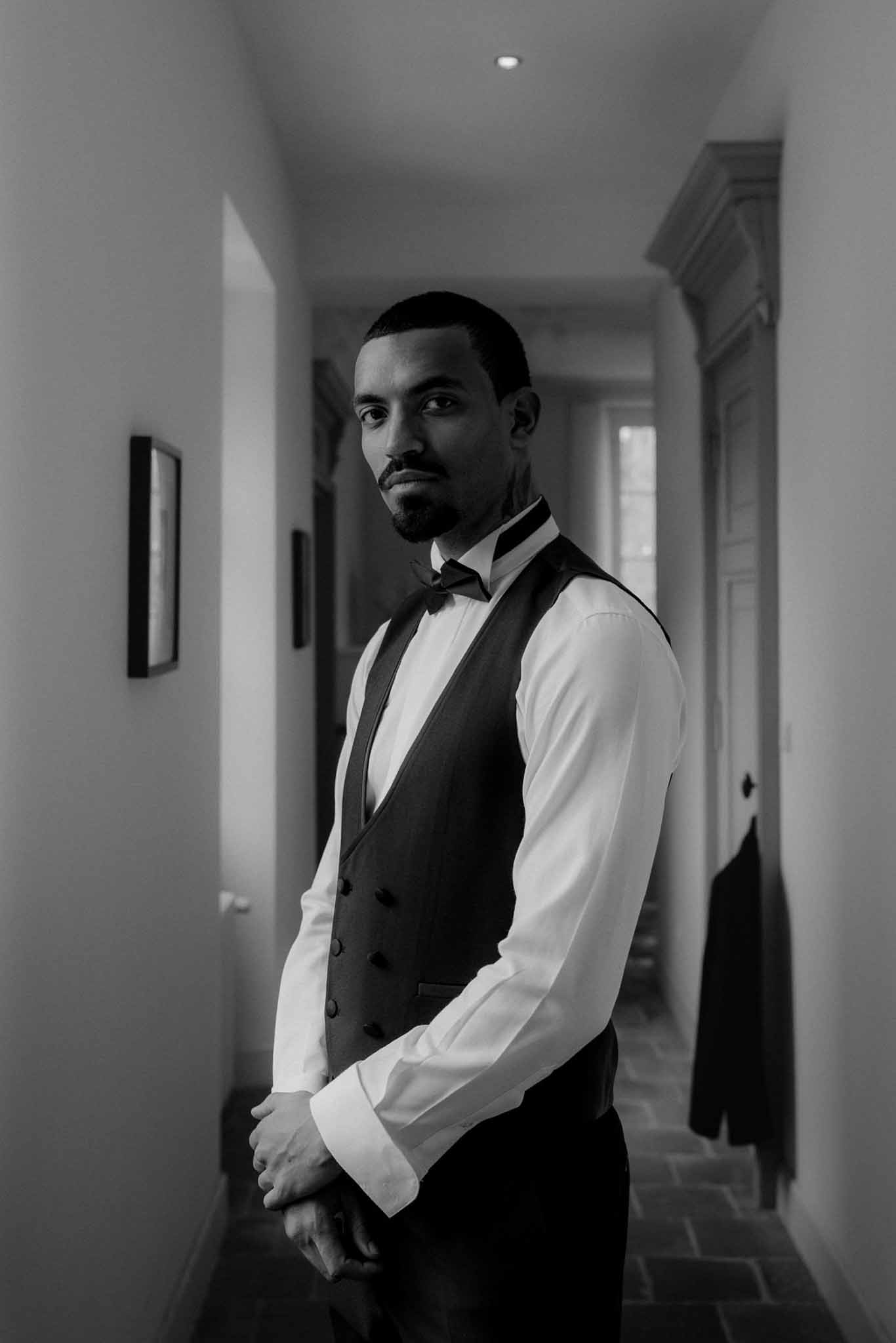 Groom in formal attire during getting ready moment in minimalist indoor hallway