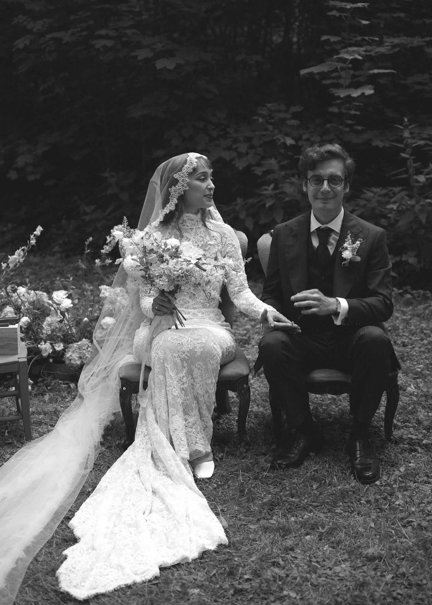 Bride and groom seated during outdoor forest ceremony with evergreen trees backdrop