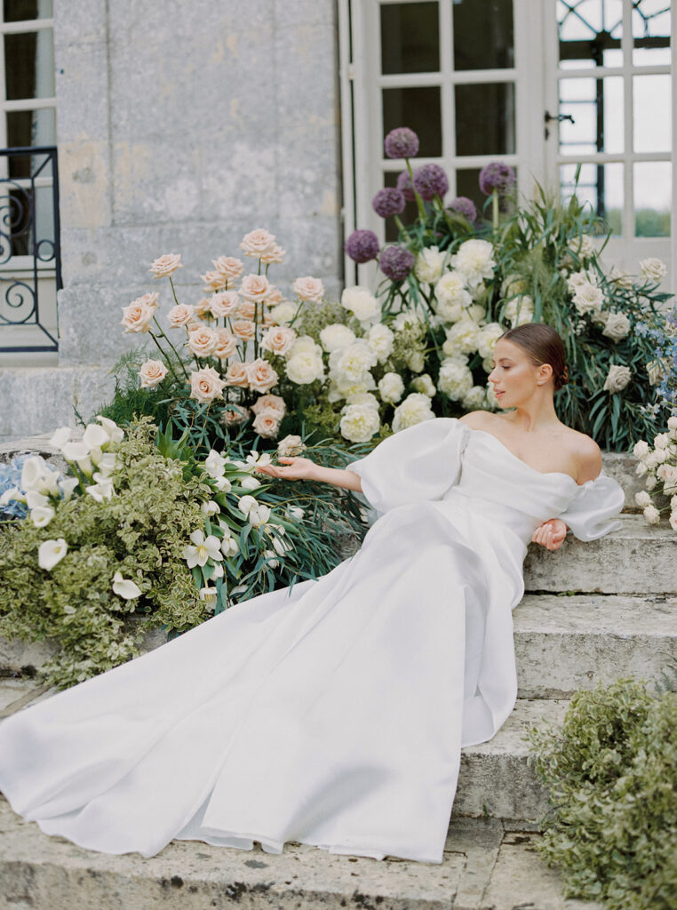 bride sitting on chateau staircase with flowers