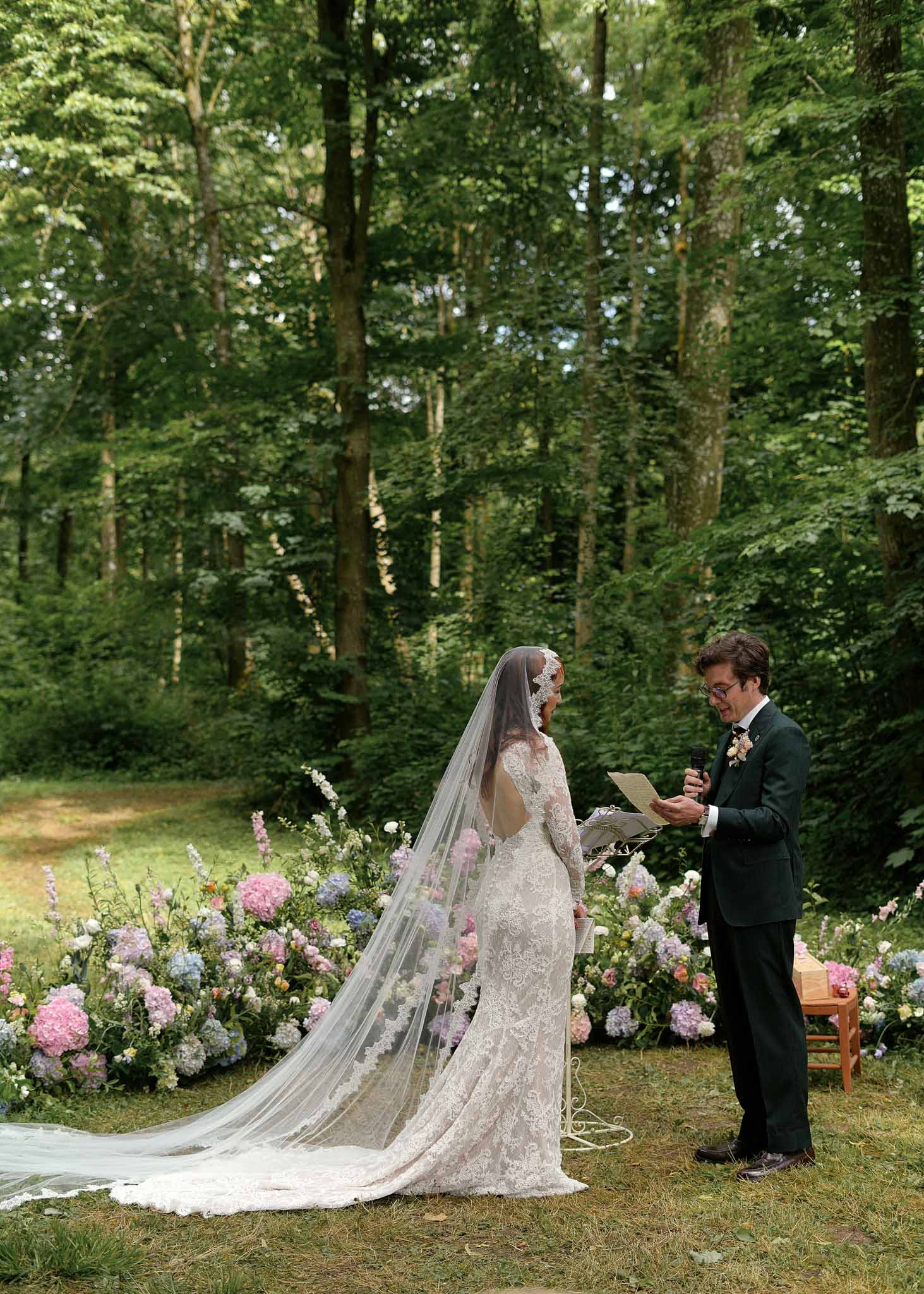 Bride and groom exchanging vows during outdoor woodland ceremony with floral arrangements